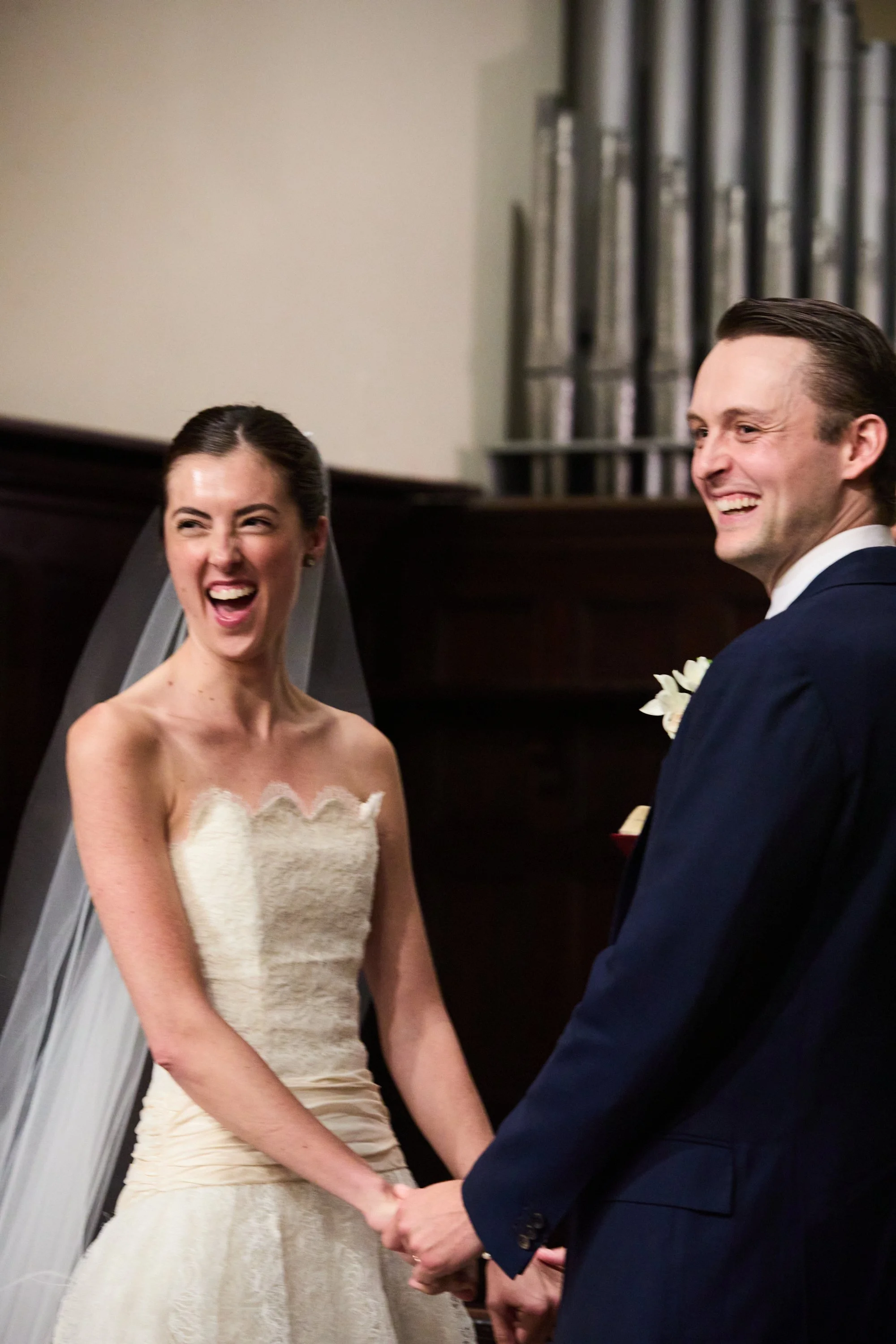 A bride and groom smiling and holding hands during their wedding ceremony indoors.