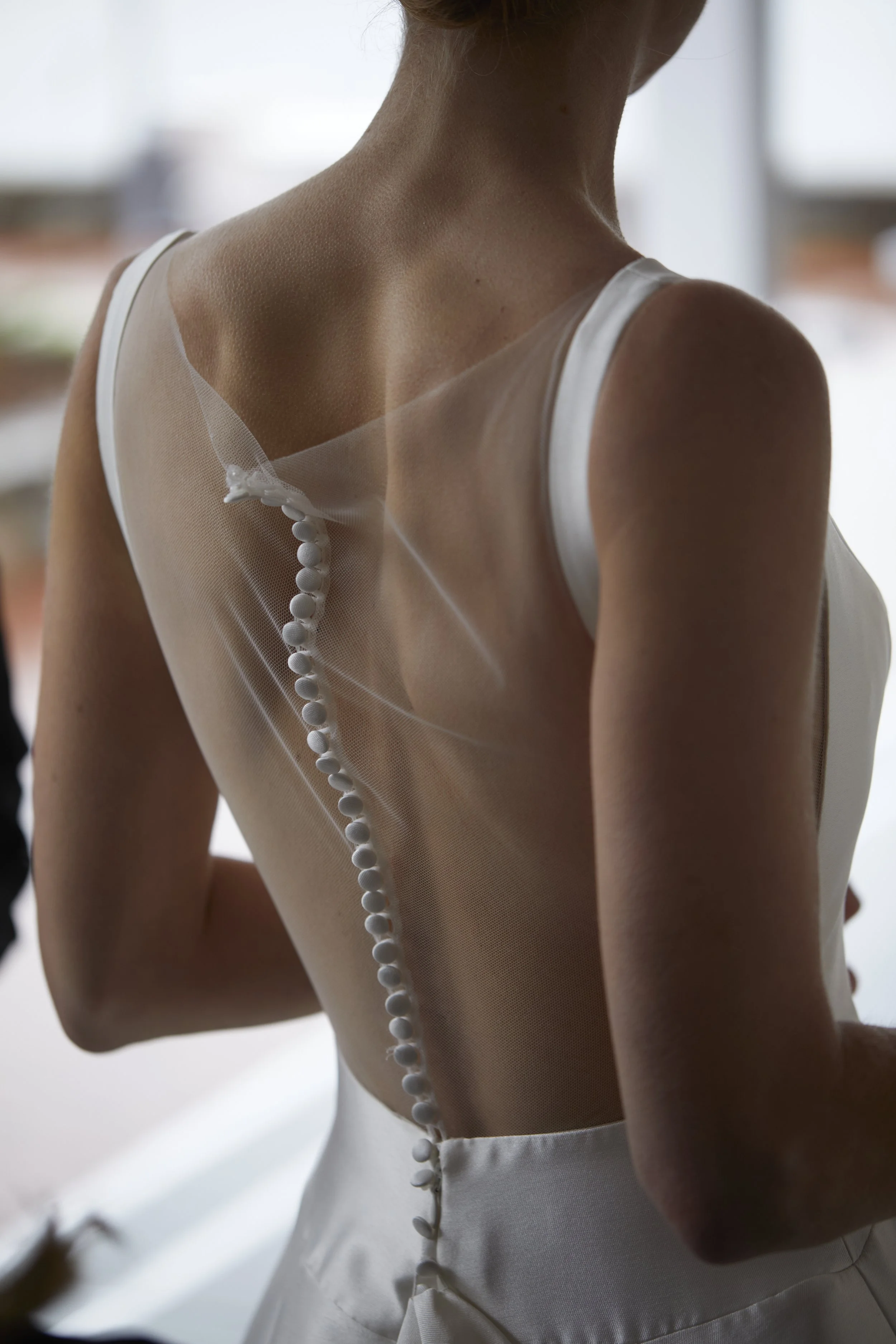 Close-up of woman in wedding dress with sheer back and white buttons.