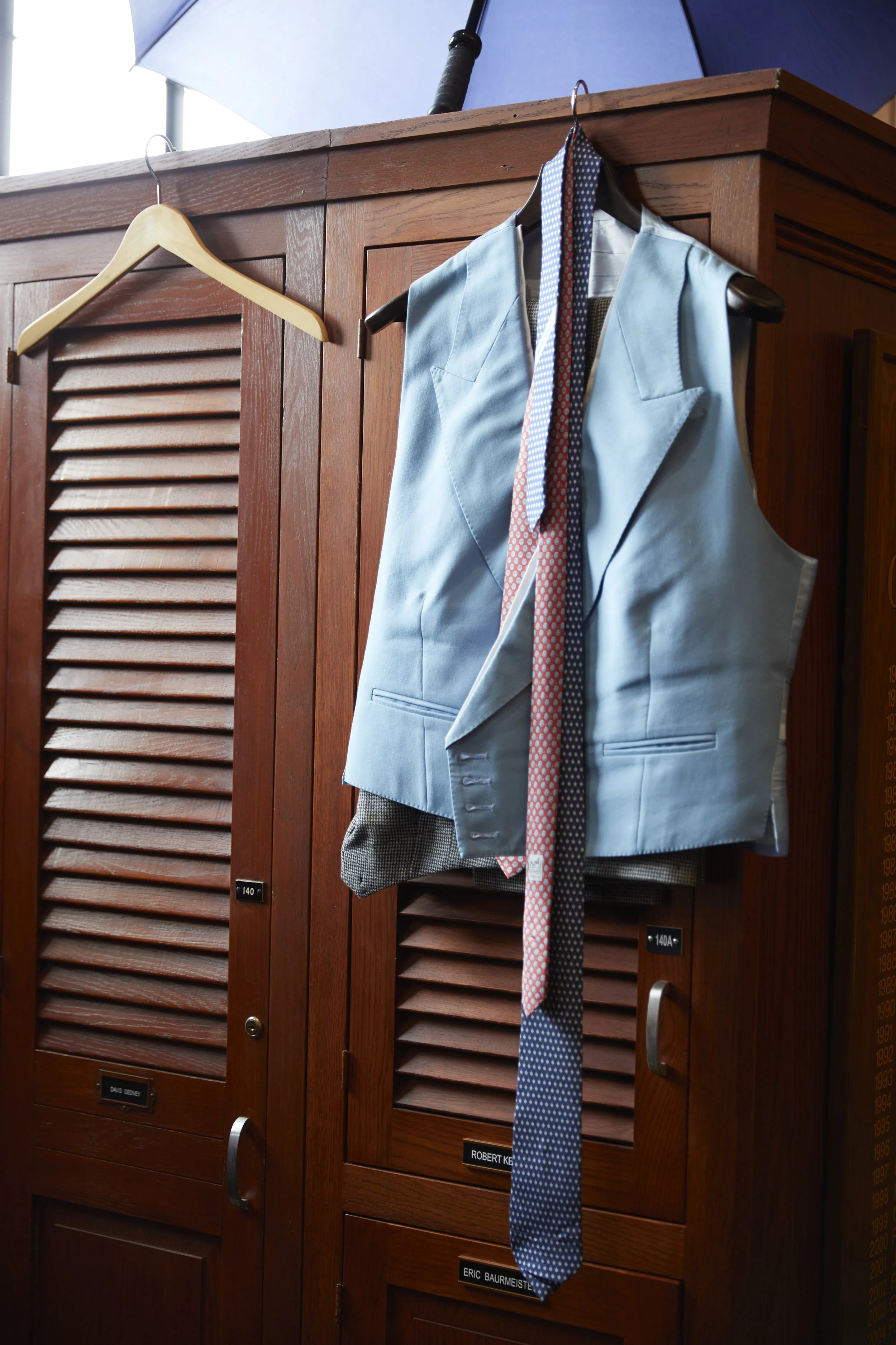 A blue vest with patterned ties hanging on a hanger on a wooden locker.