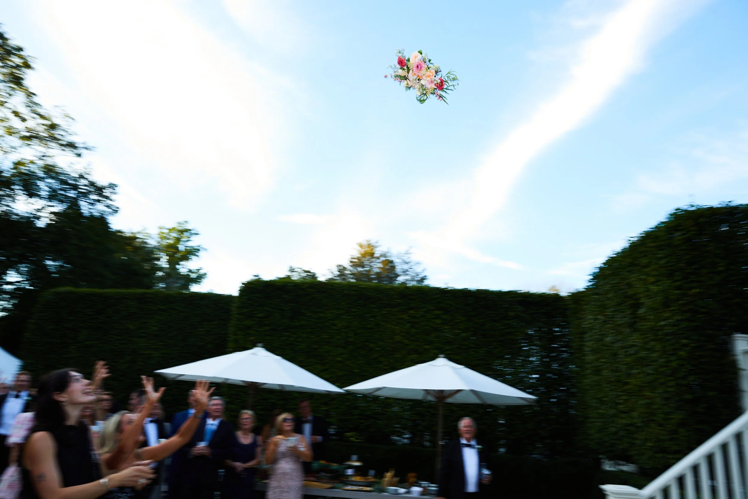 People at an outdoor celebration throwing a flower bouquet into the sky.