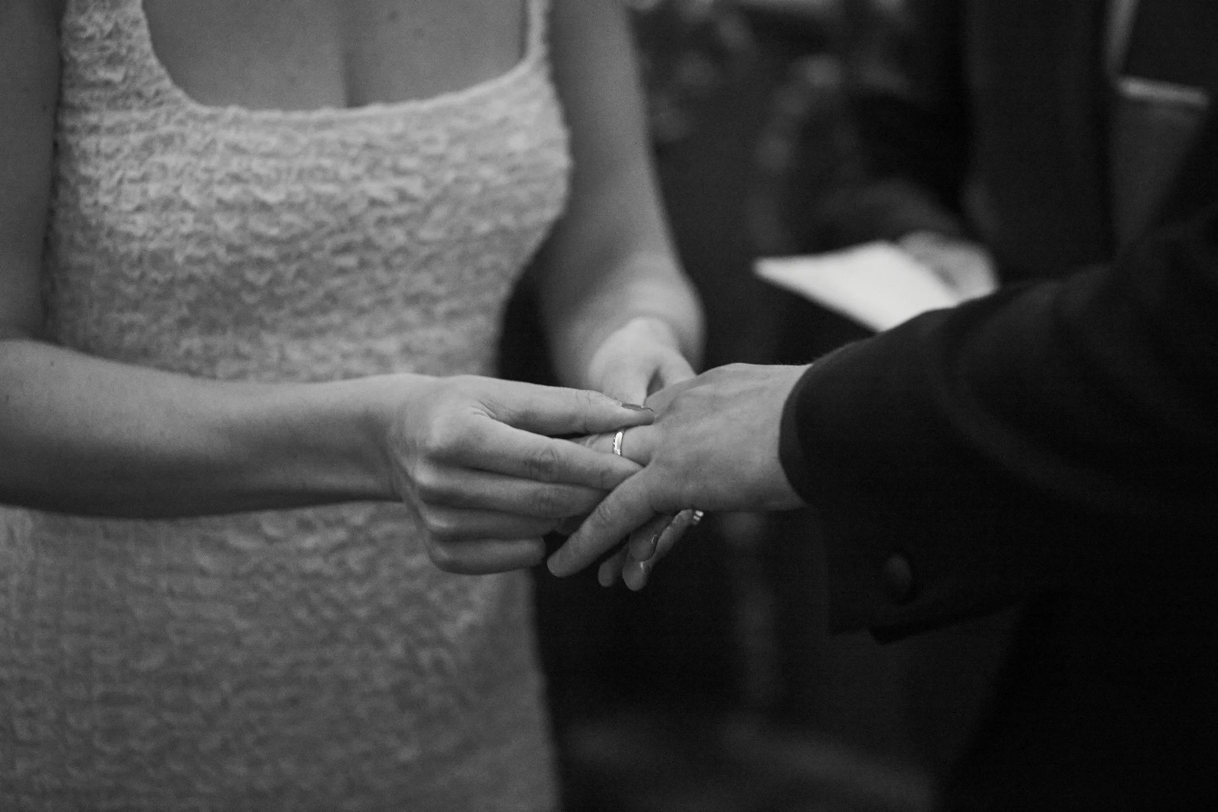 Two people holding hands during a wedding ceremony, with a focus on their hands and rings.