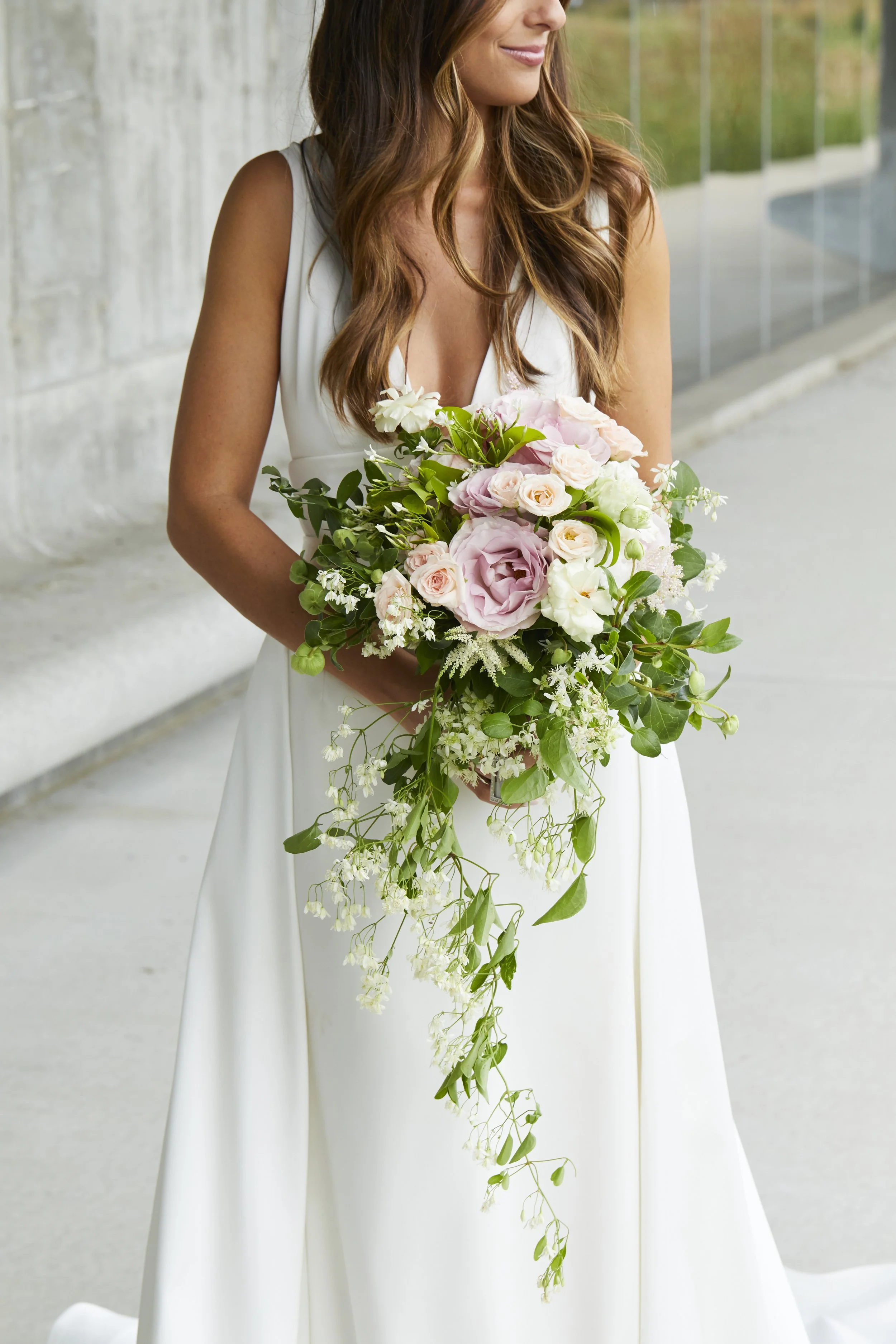 A woman in a white dress holding a cascading bouquet of pink and white roses, greenery, and white flowers.