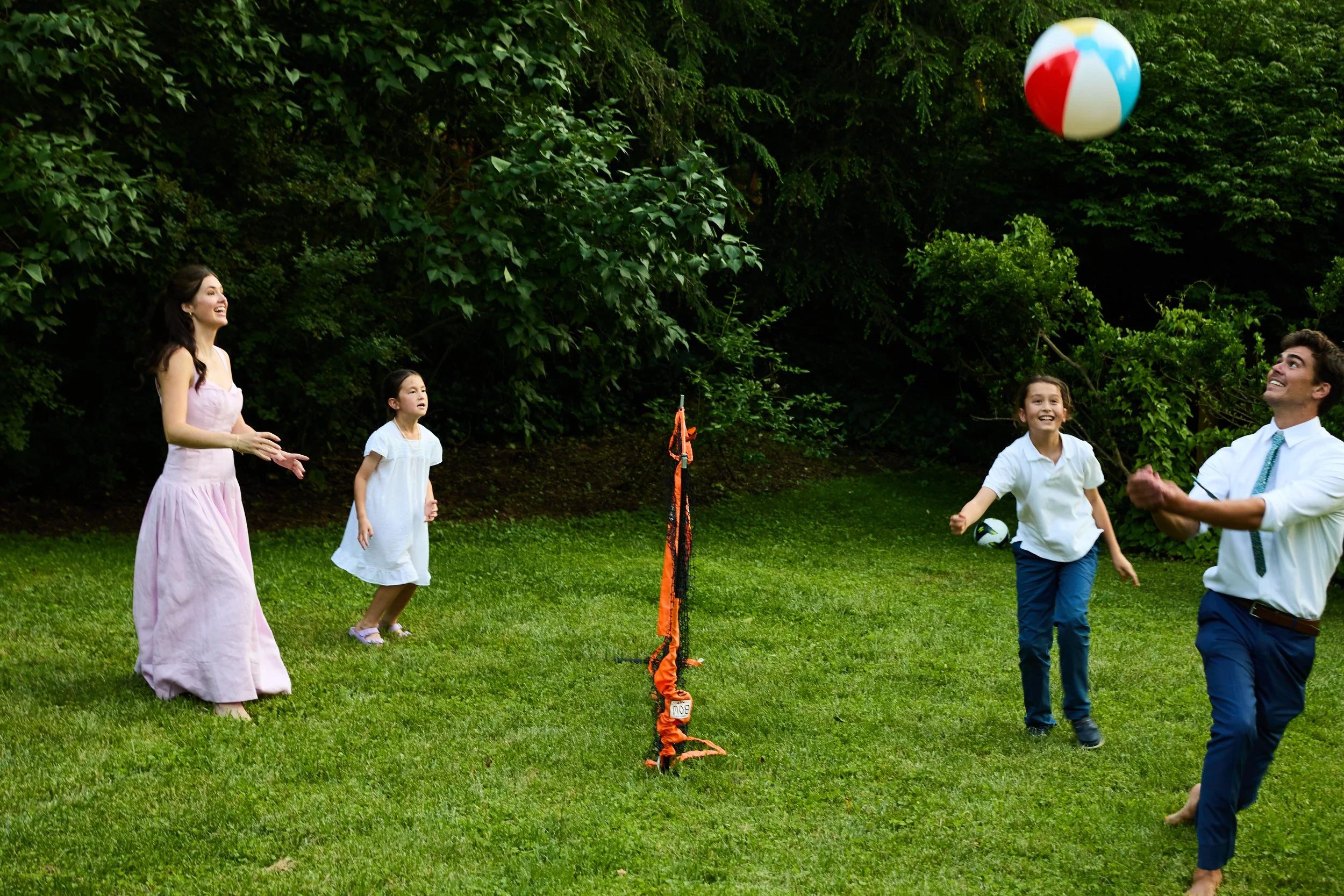 A family playing with a beach ball outdoors on a grassy lawn, with children and adults smiling and enjoying a sunny day.