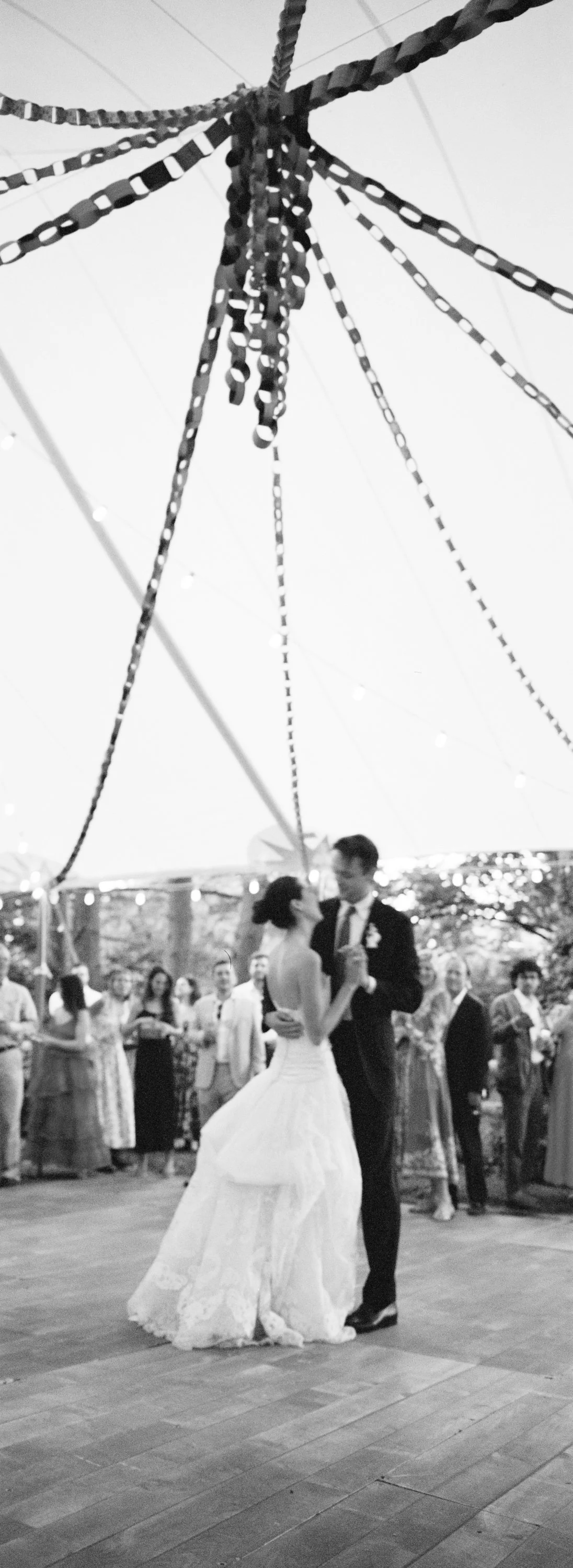 A bride and groom dancing at their wedding reception under a canopy of decorative hanging ribbons, with guests watching in the background.