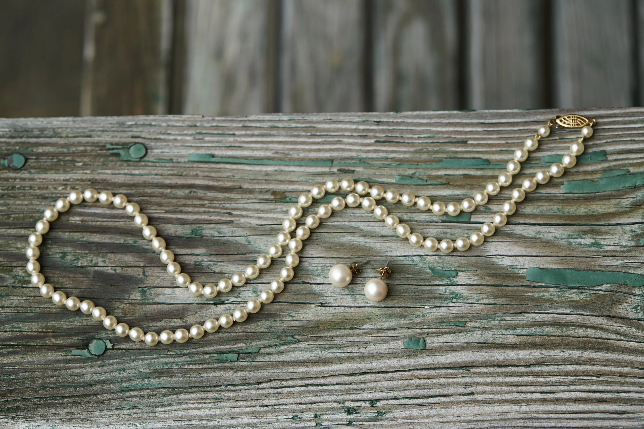 Pearl necklace and matching pearl earrings on weathered wooden surface.