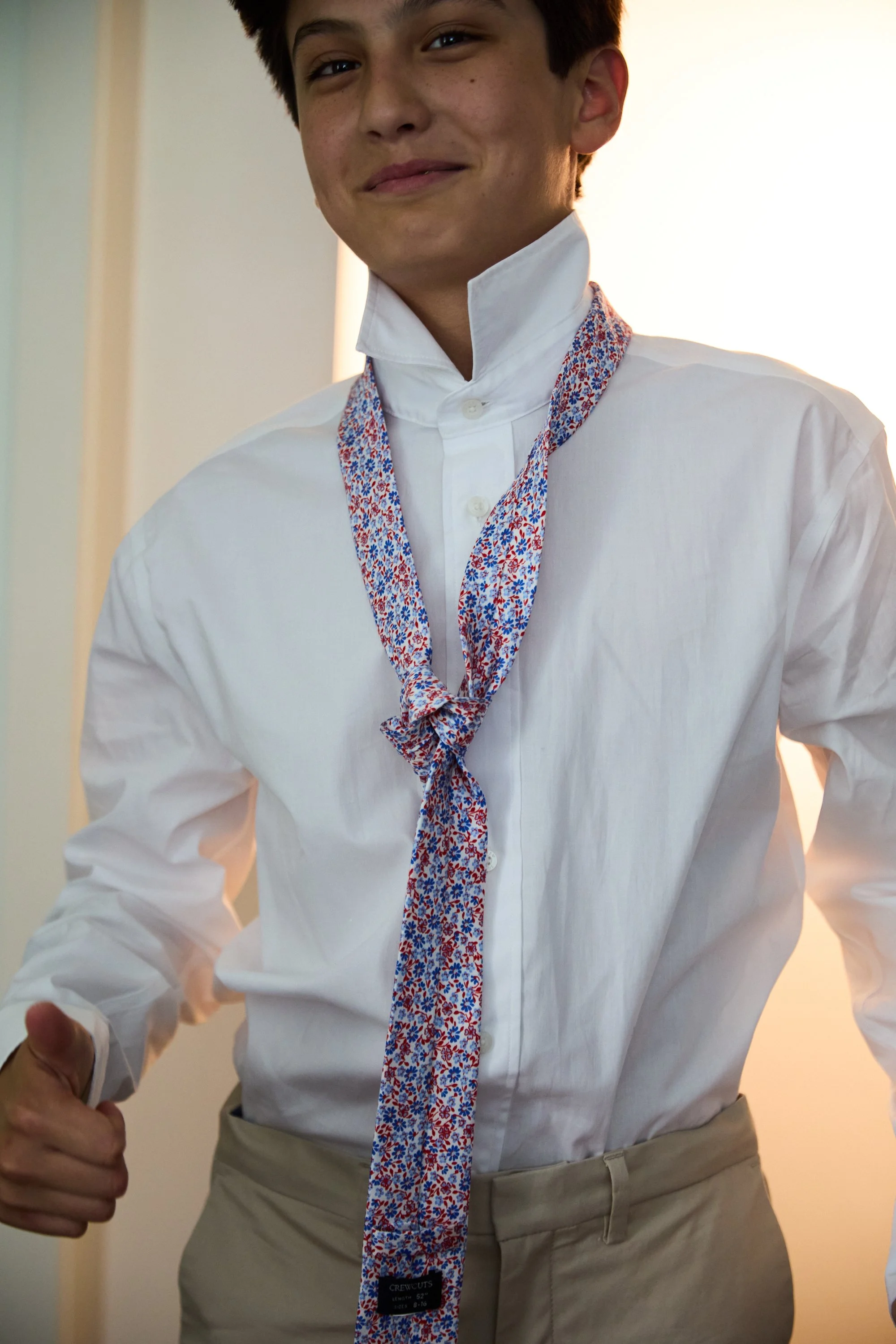 A young man is dressed in a white button-up shirt with a colorful floral necktie around his neck.