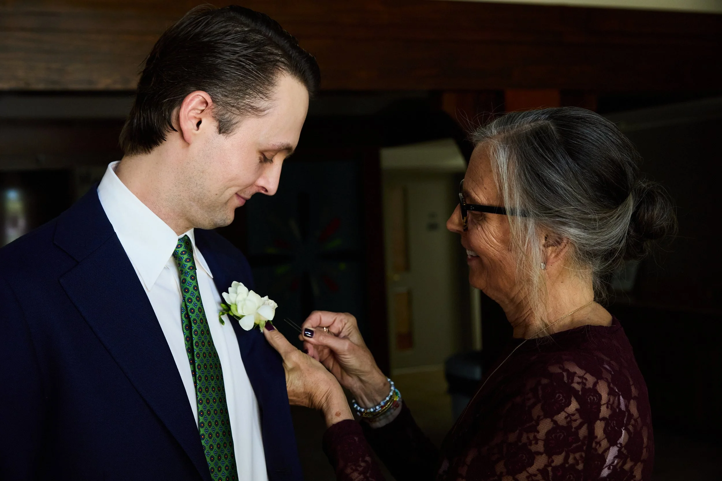 An elderly woman pinning a white boutonniere onto a young man's suit at a formal event