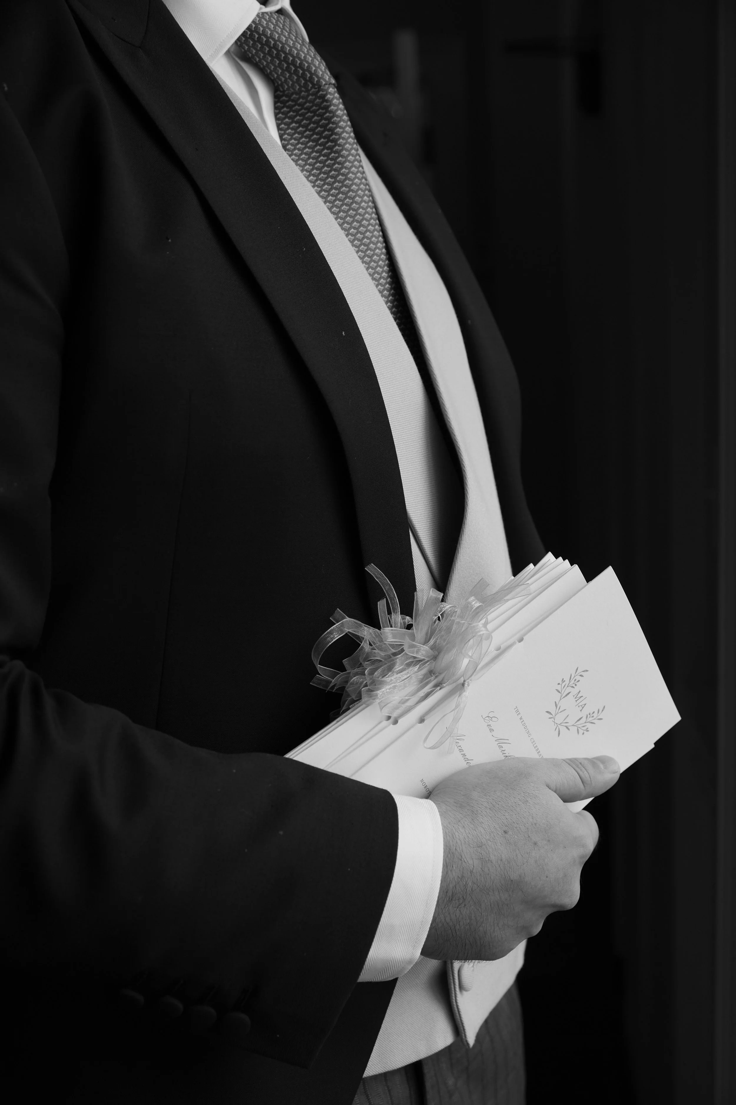 A man in a suit holding wedding programs decorated with a ribbon.