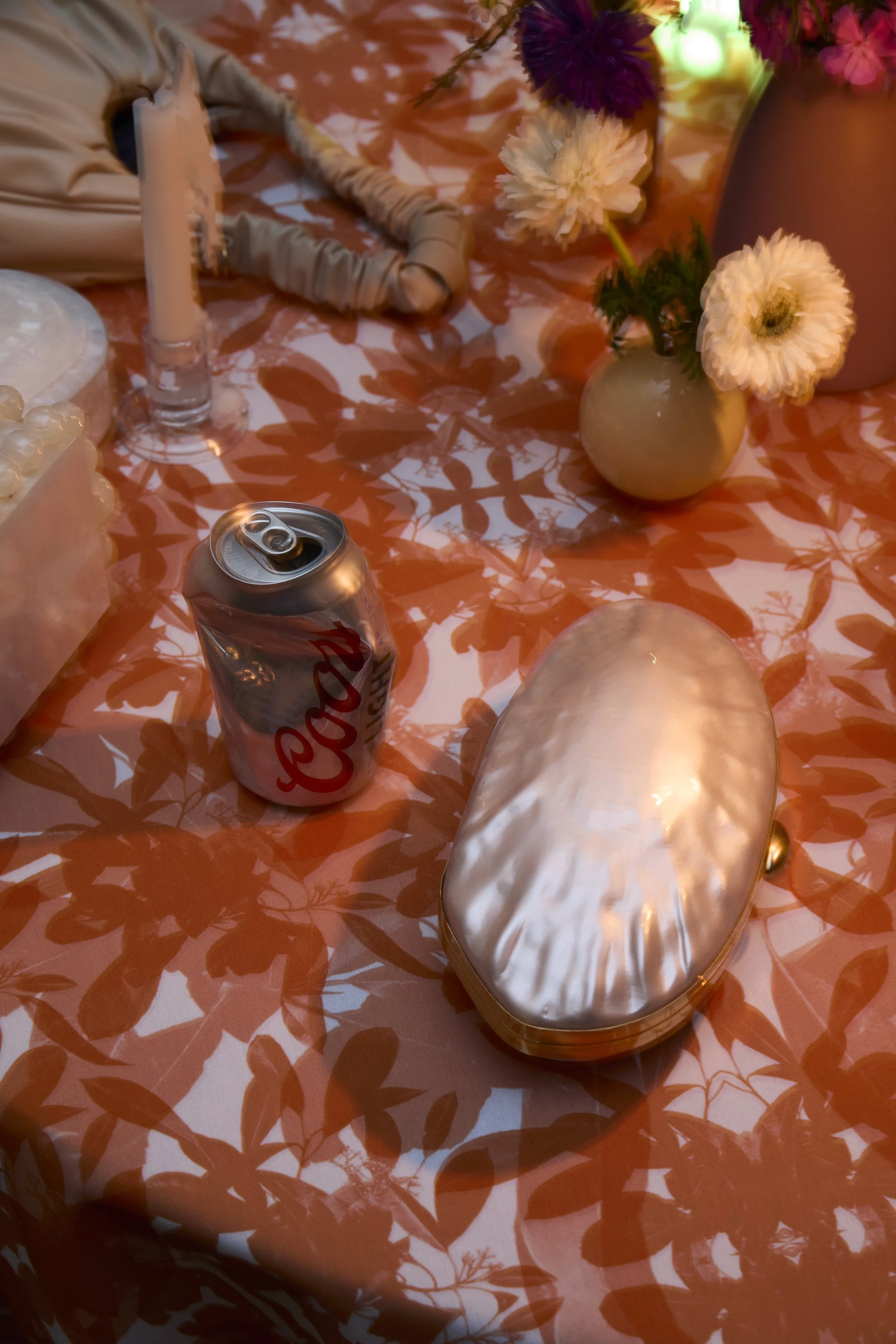 A table decorated with flowers, a pearl clutch, a can of Coca-Cola, a candle, and other decorative items.