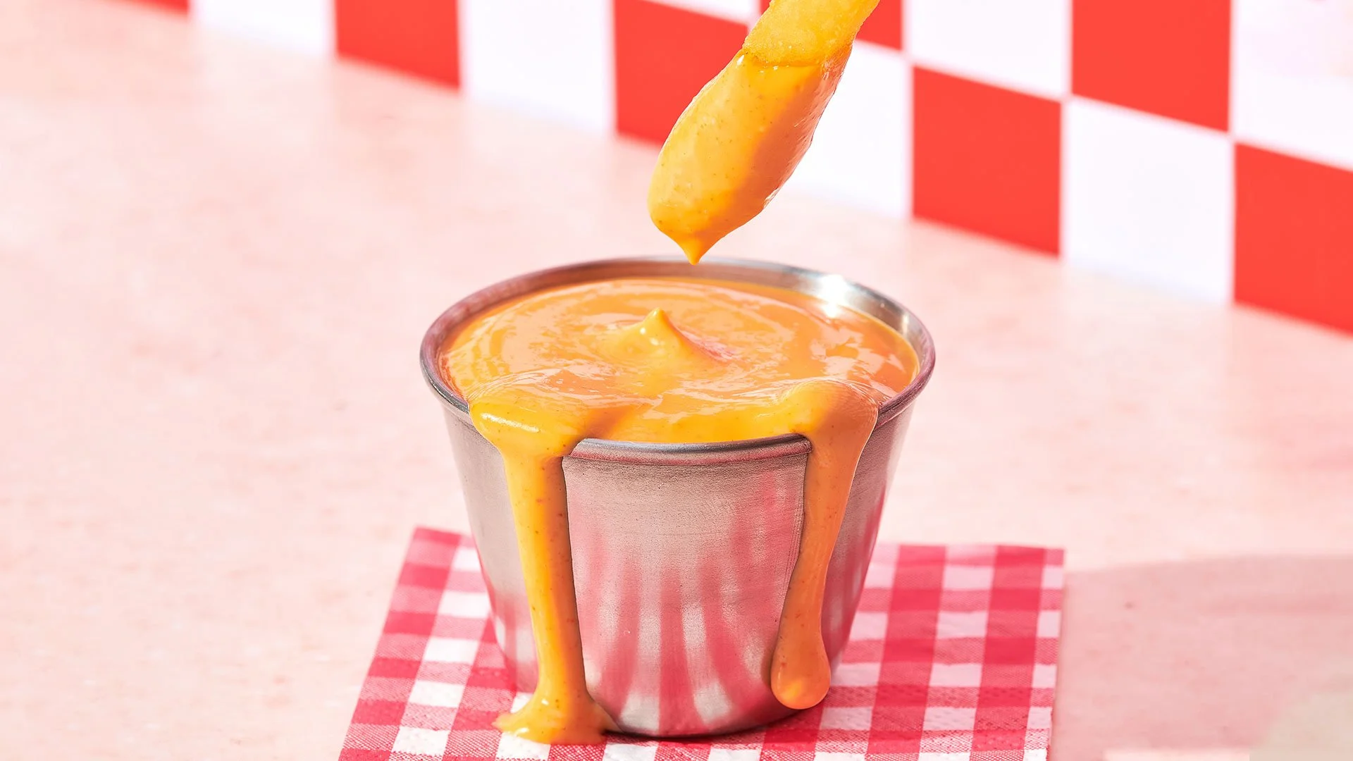A metal cup filled with melted cheese, with cheese dripping over the sides, and a piece of bread or cheese being dipped into it.