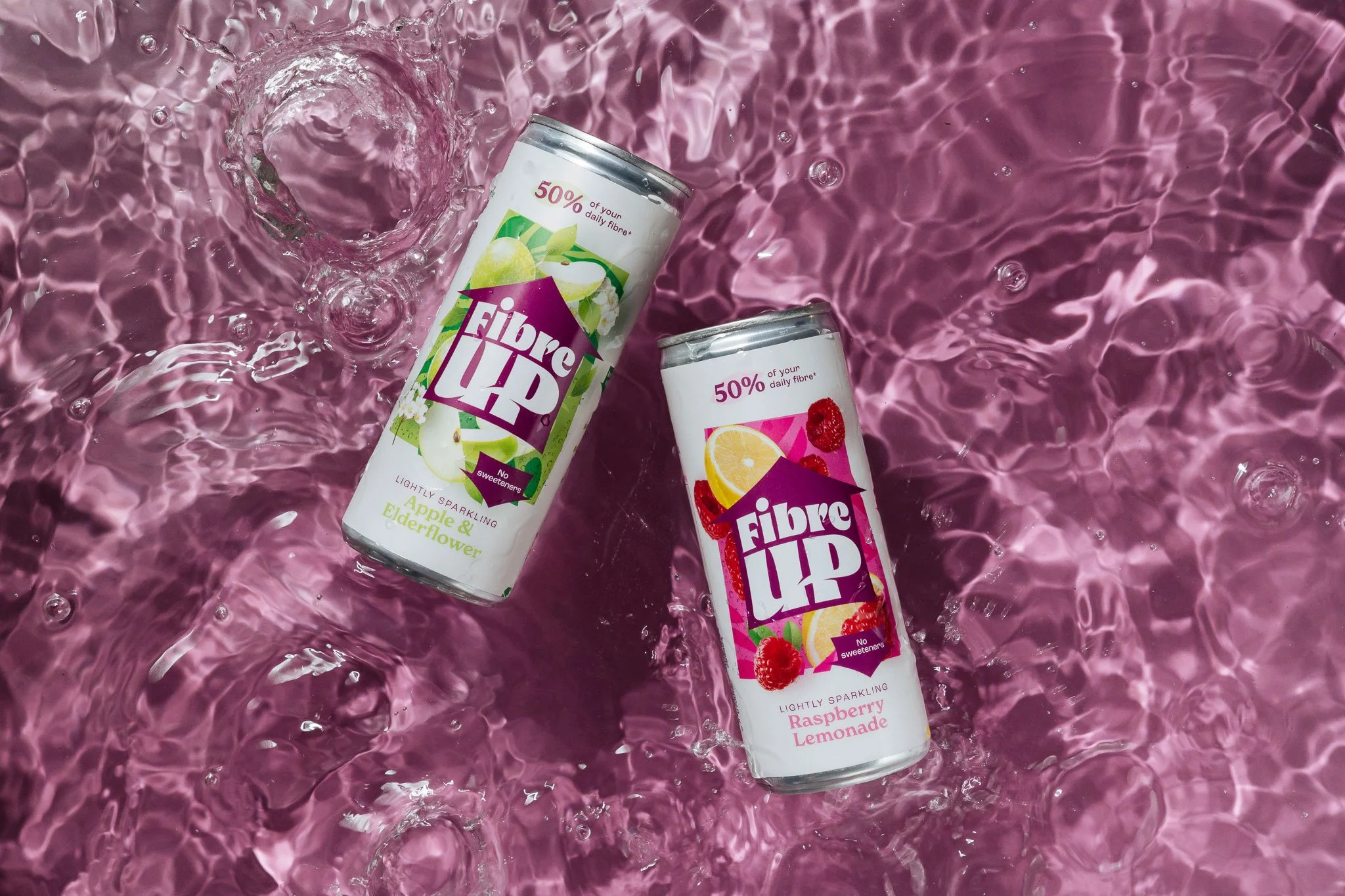 Two cans of Fibre UP sparkling beverages with apple and elderflower flavor and raspberry lemonade flavor, floating in pink water.