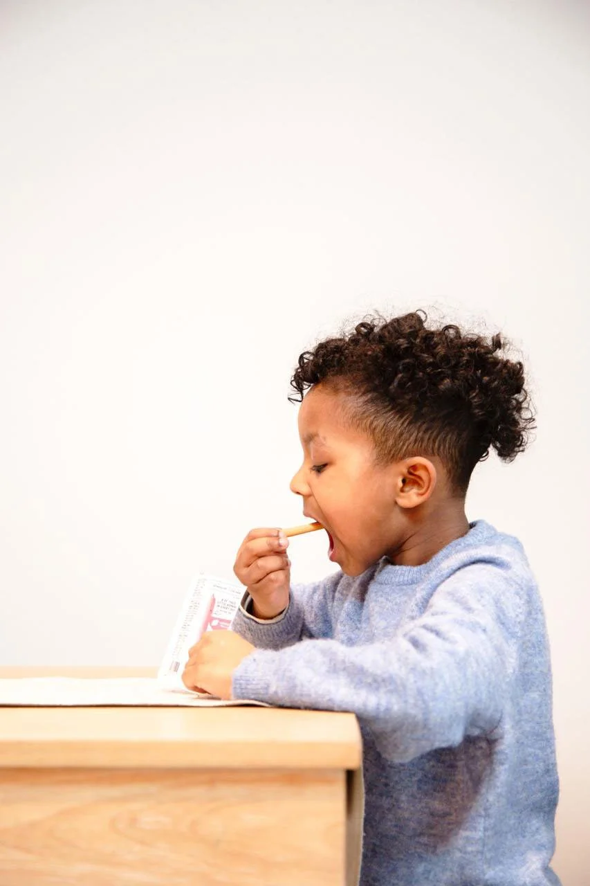 A young child with curly hair eating a snack at a table.
