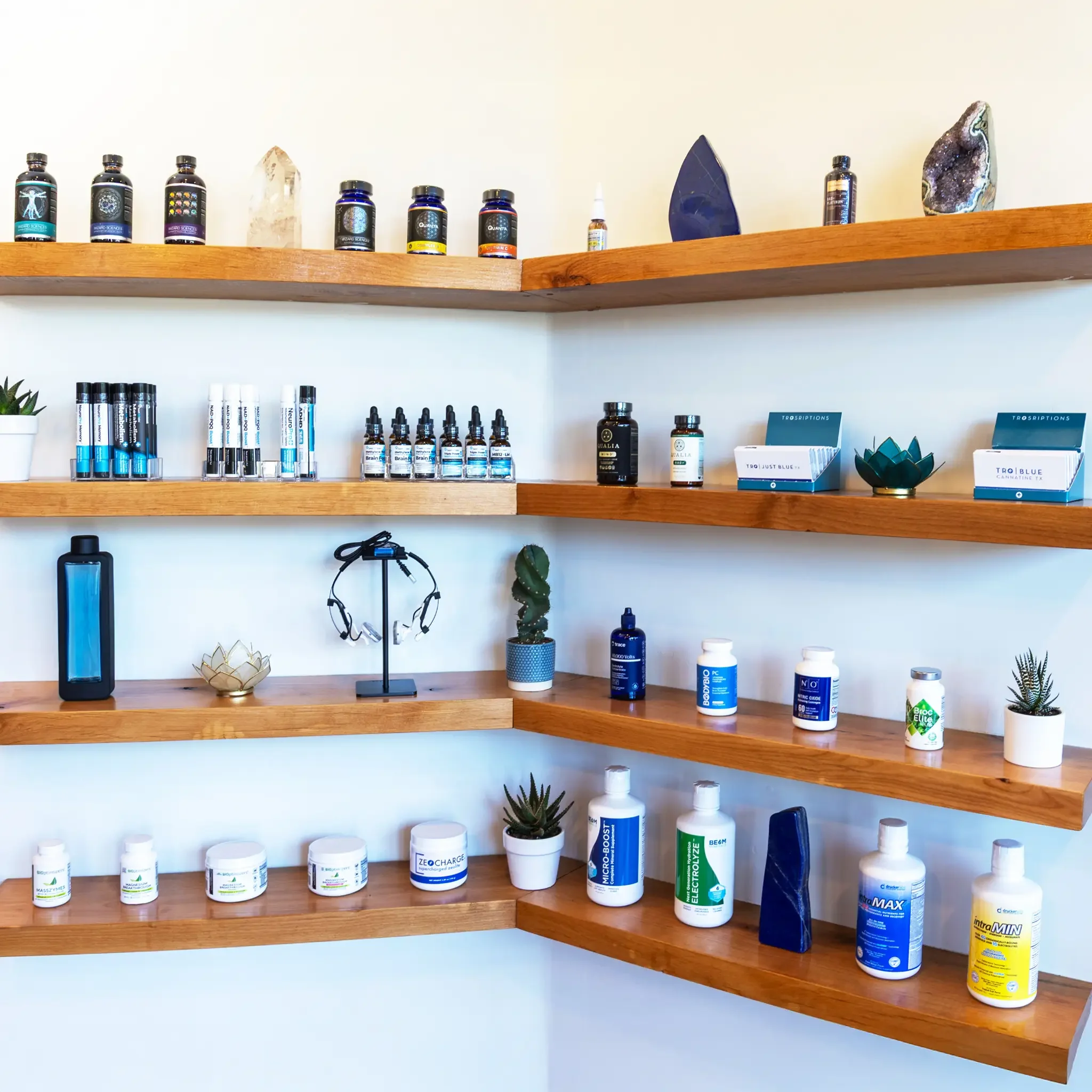 Wooden shelves hold various bottles and containers, including health supplements, essential oils, crystals, and plants, arranged in a tidy display.