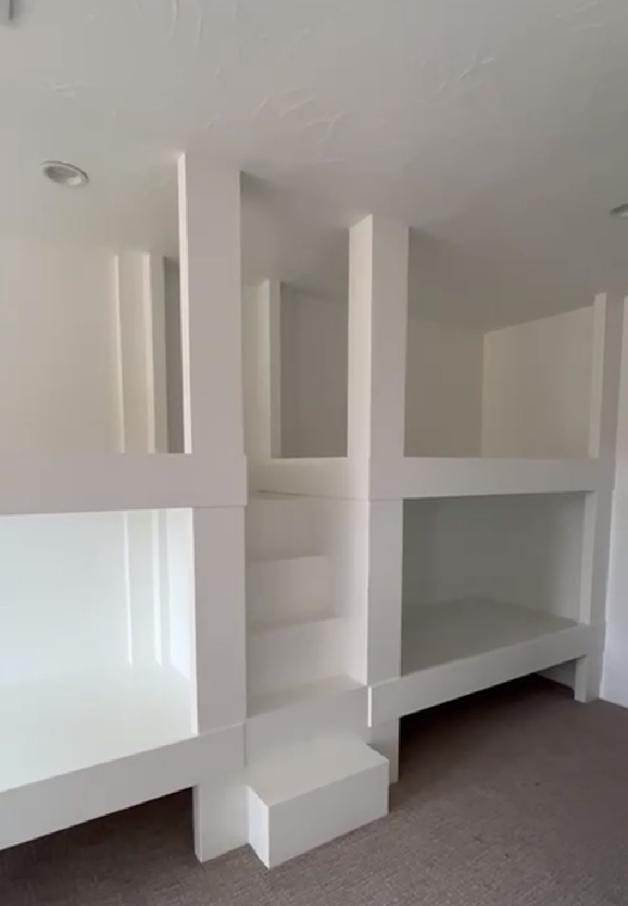 White built-in shelving unit with open cubbies and a step, installed against a wall in a room with carpeted floor.