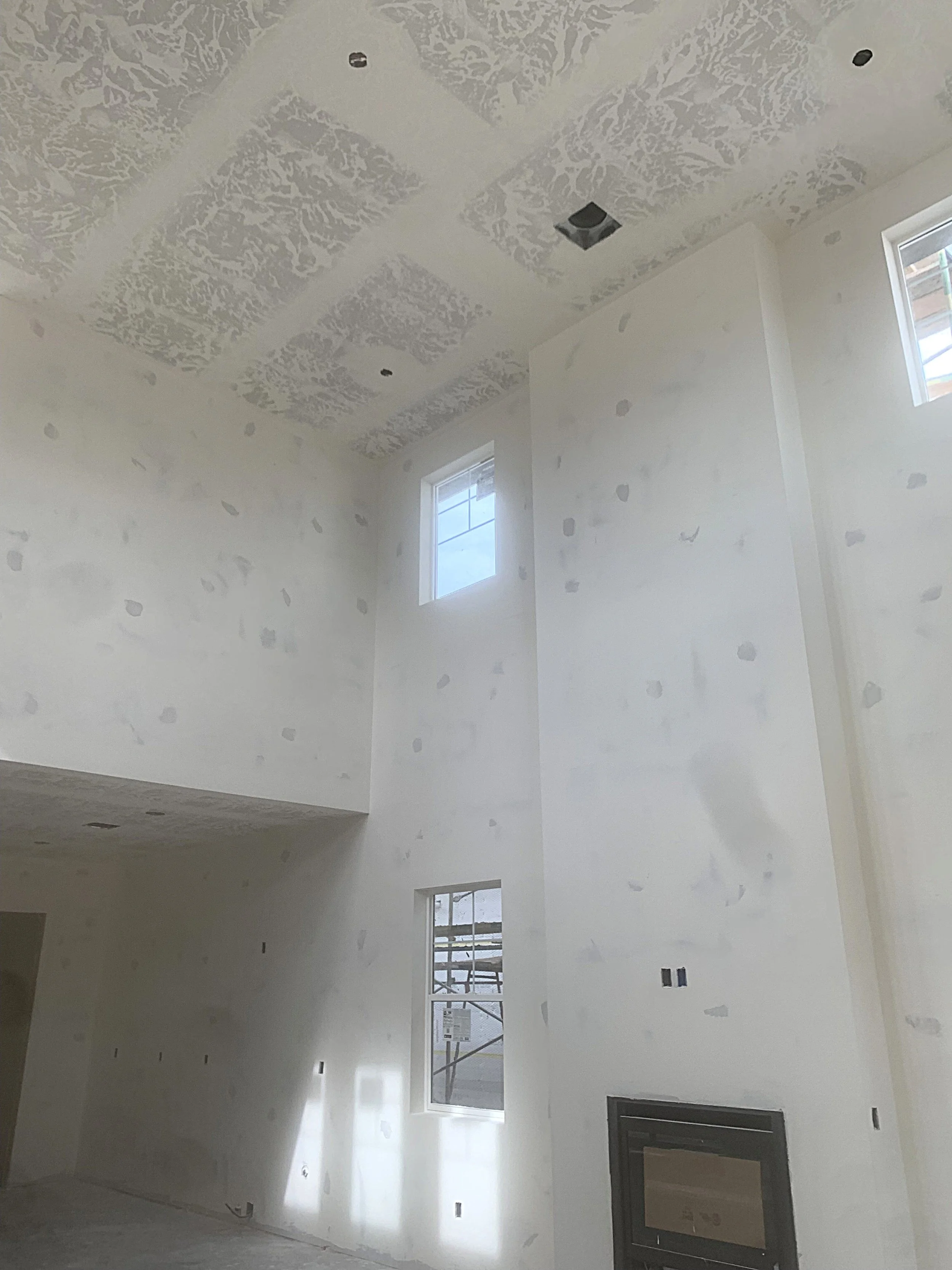 Interior of a new house under construction, with unfinished white walls, high ceiling, and multiple windows.