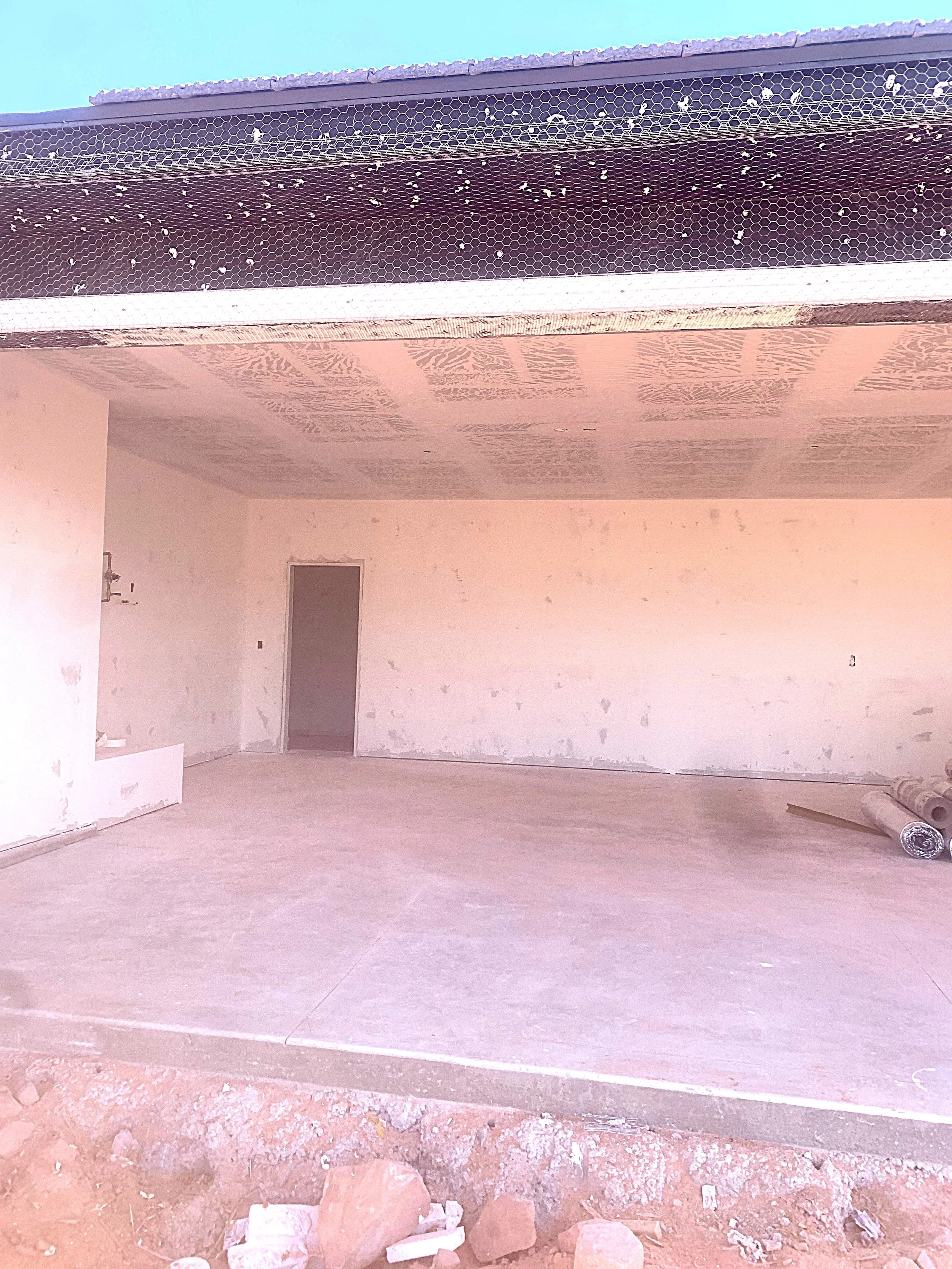 Empty room under construction with unfinished walls and a concrete floor, some rolled-up materials on the right, and rocks at the front exterior.