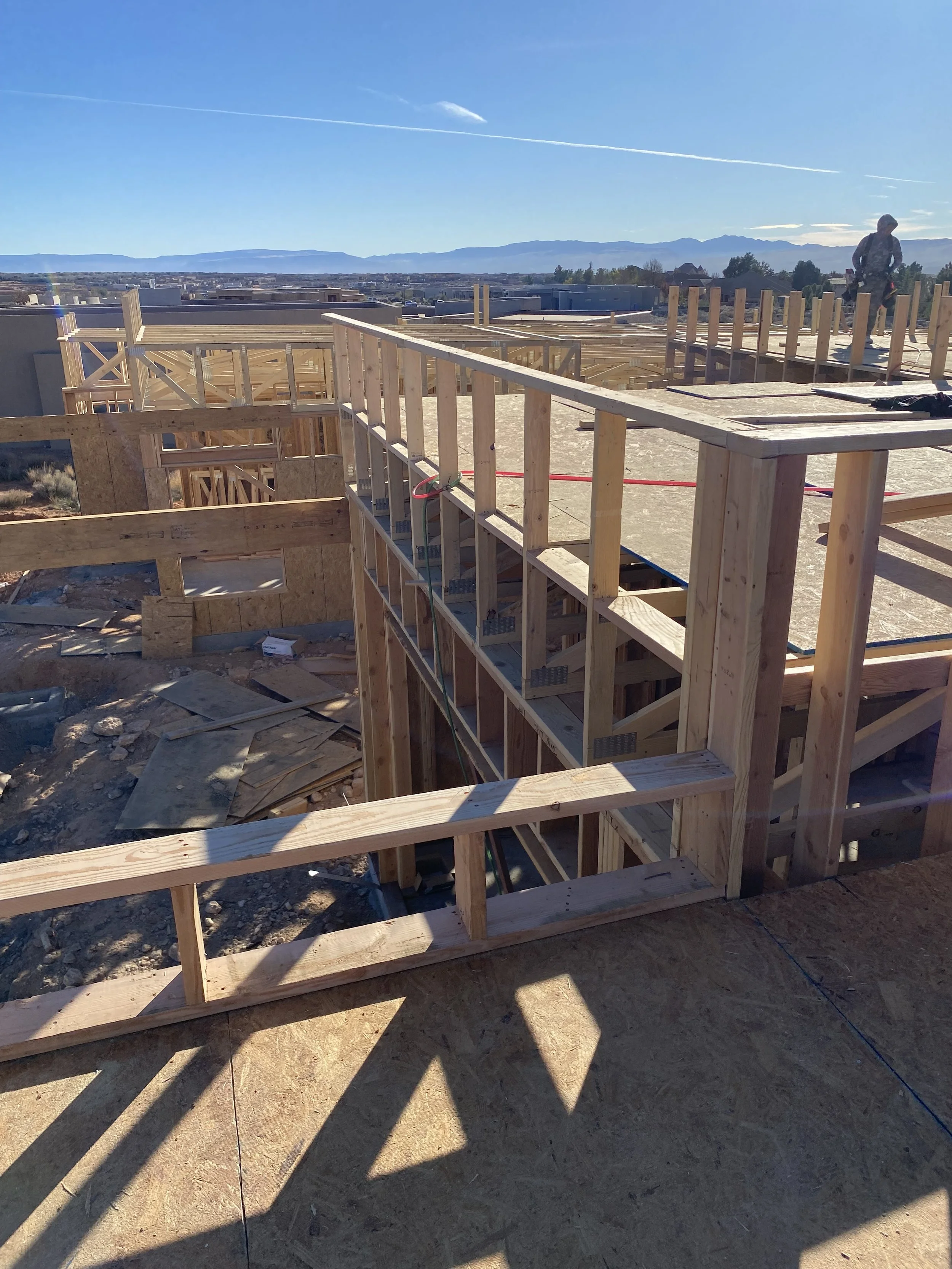 Construction site with wooden framing on a building, with a person working in the distance under a clear blue sky.