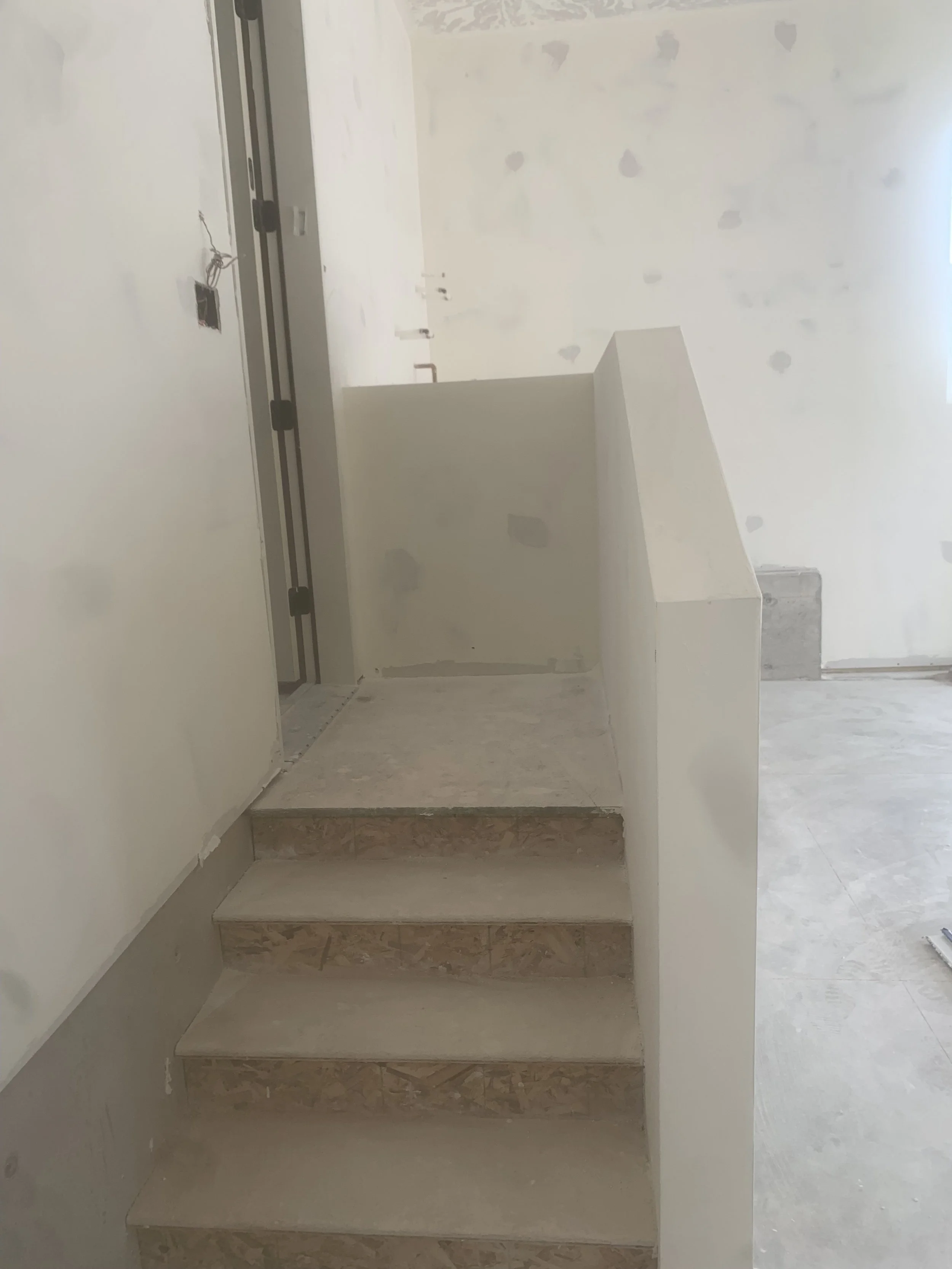 Construction site with unfinished interior, small staircase leading to an open ceiling and partially painted walls.