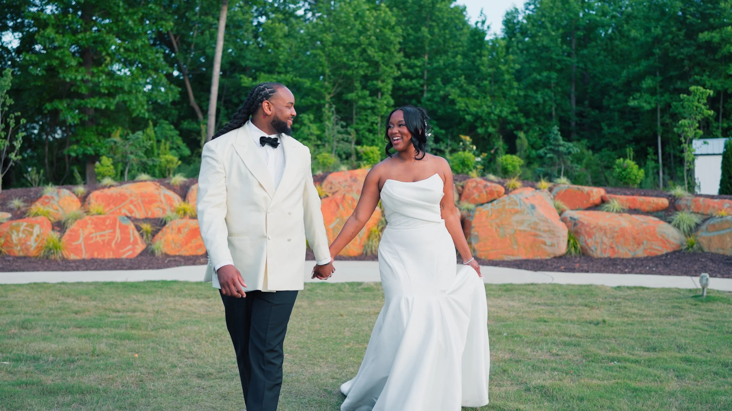 A couple in wedding attire sharing an intimate moment outdoors at sunset, with trees in the background.