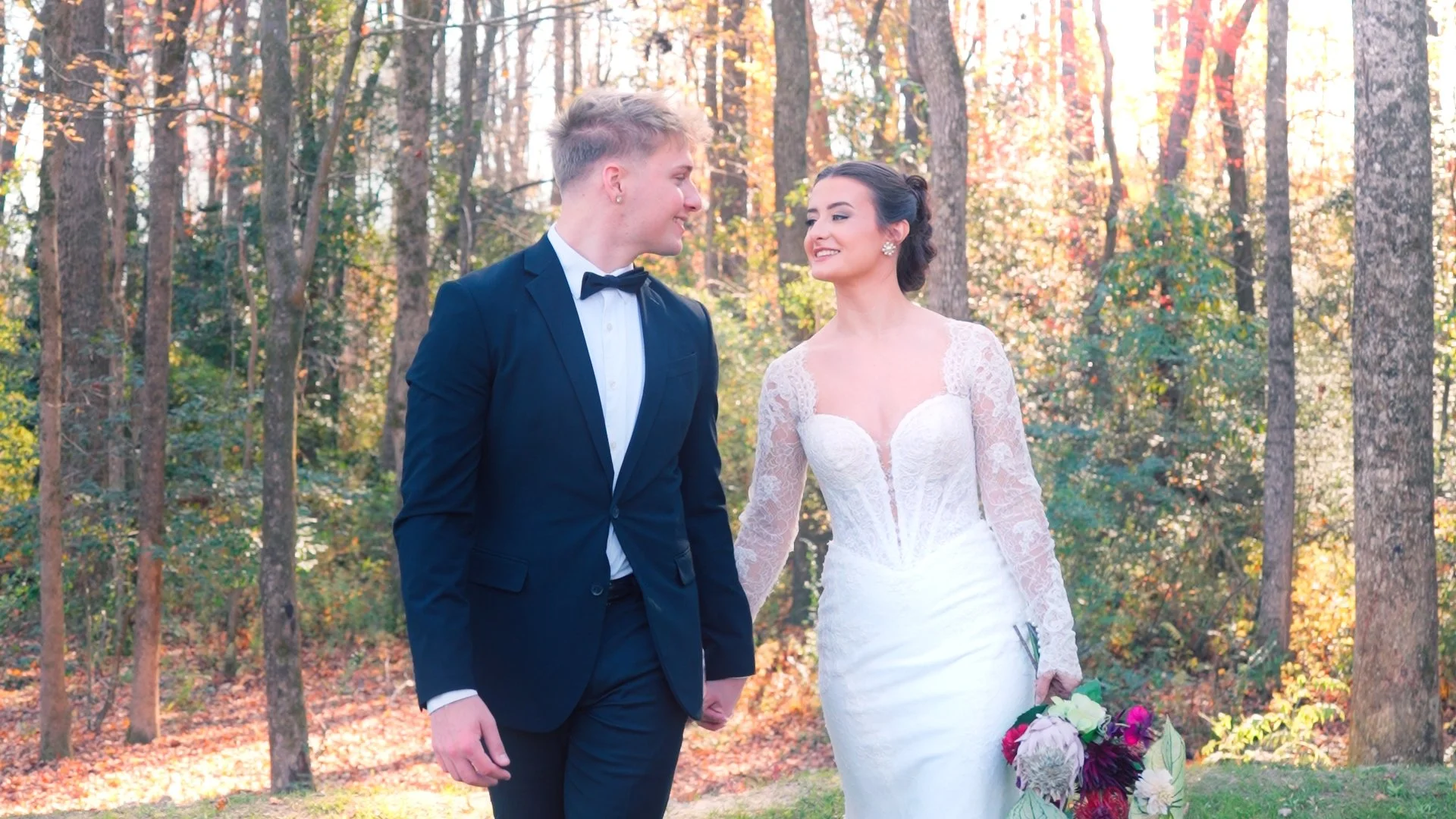 A happy bride and groom holding hands and walking through a sunflower field on a sunny day.