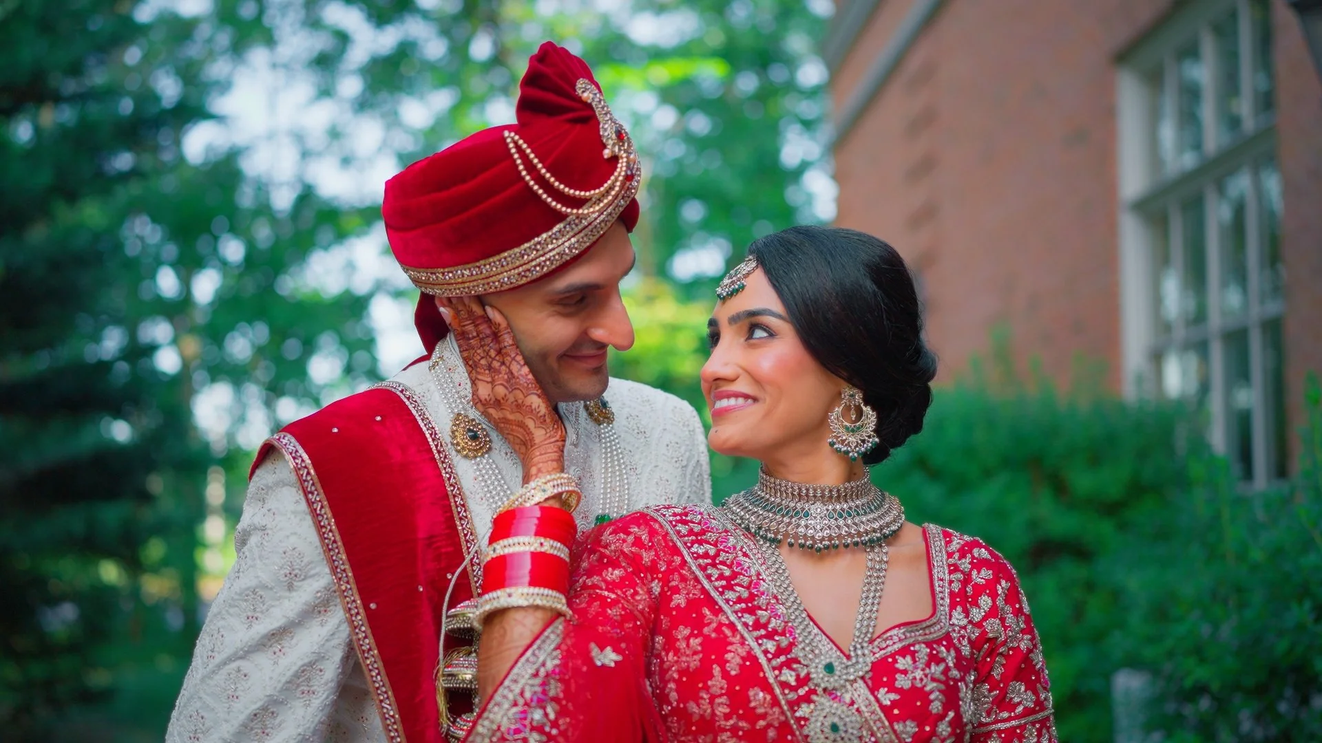 A couple in wedding attire sharing an intimate moment outdoors at sunset, with trees in the background.
