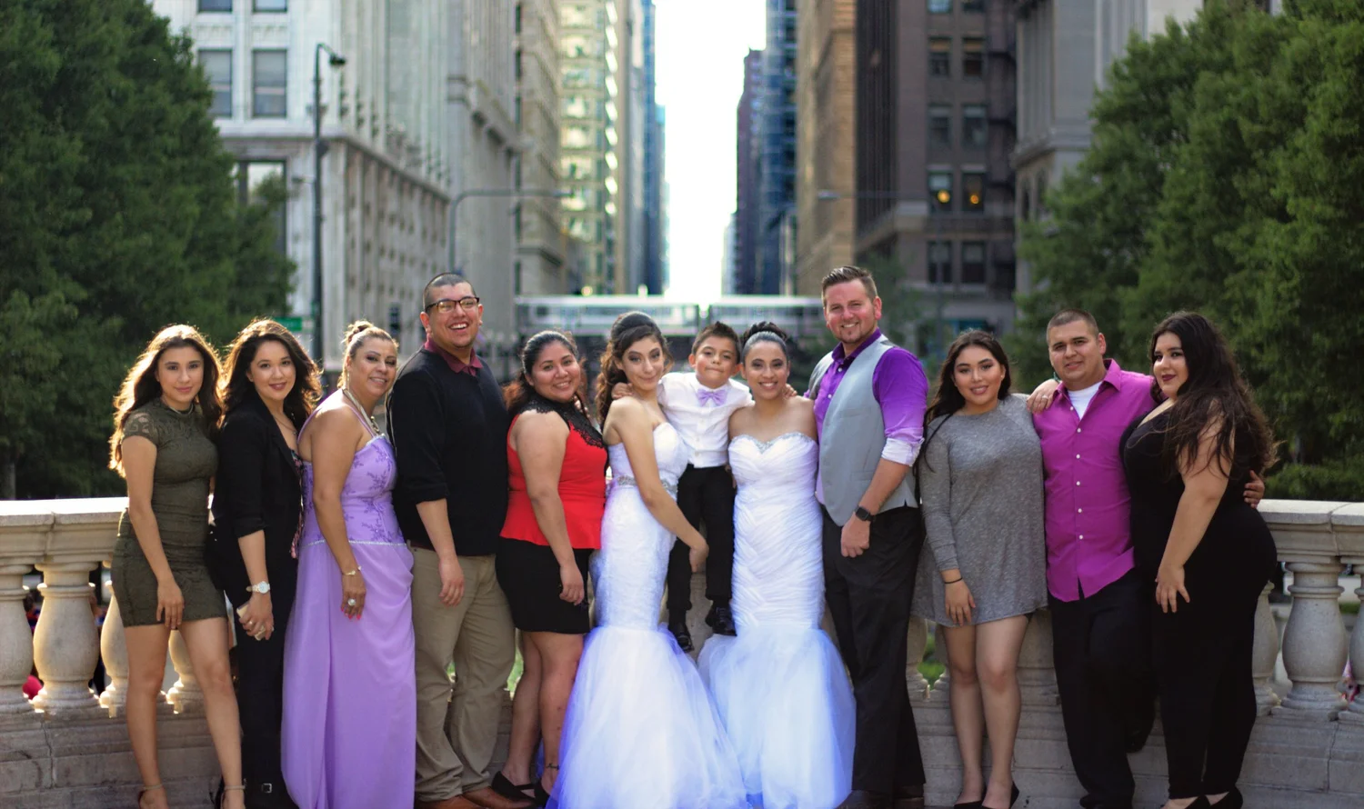 A wedding party gathered beside a balustrade with city buildings in the background