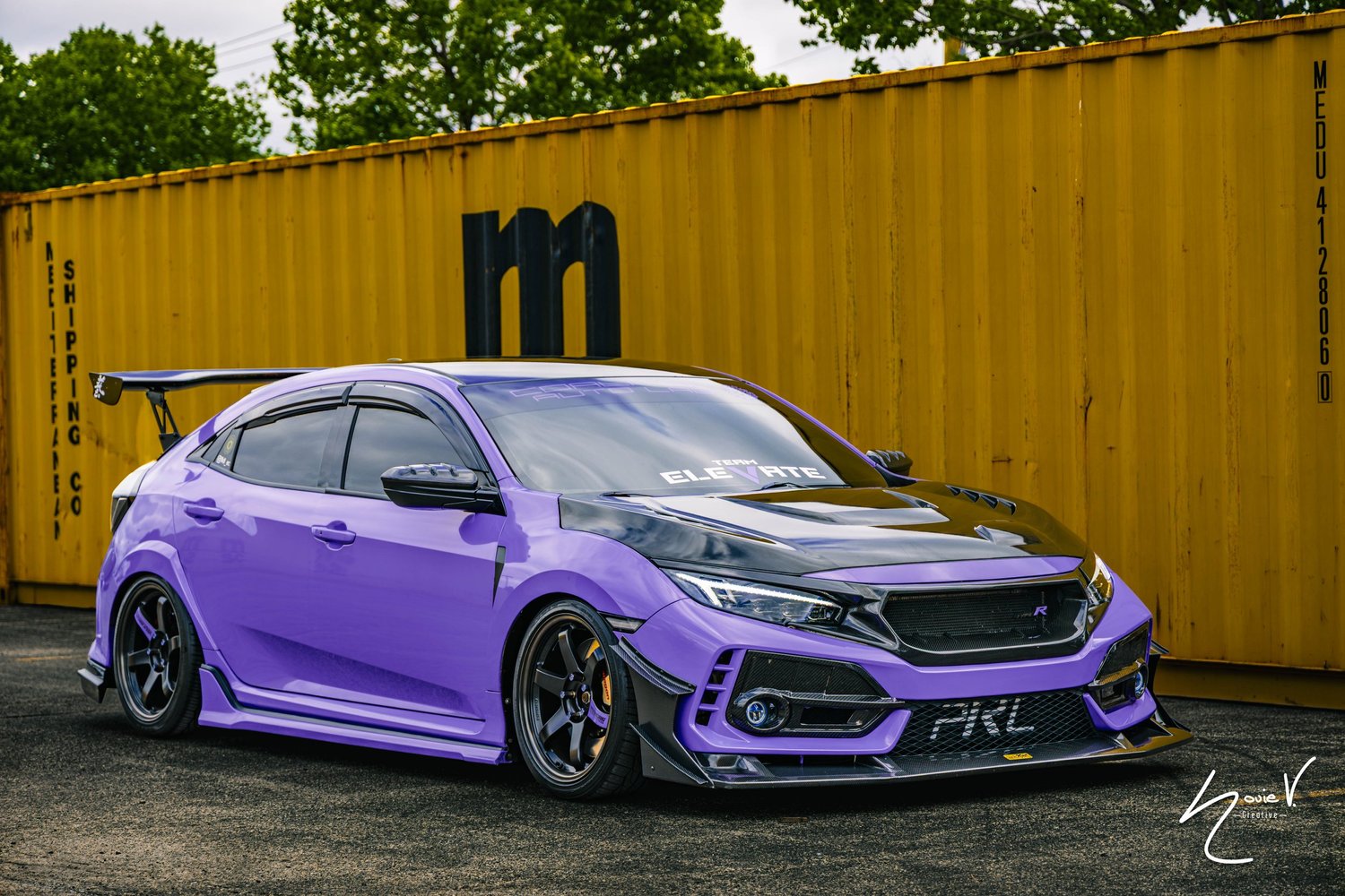 A purple car parked in front of a yellow shipping container
