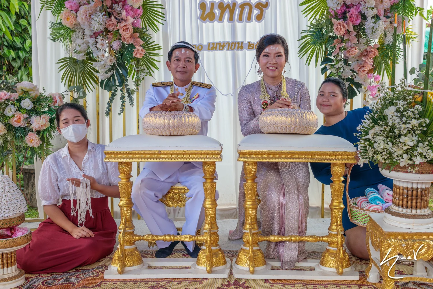 A couple at a wedding ceremony surrounded by family and floral arrangements