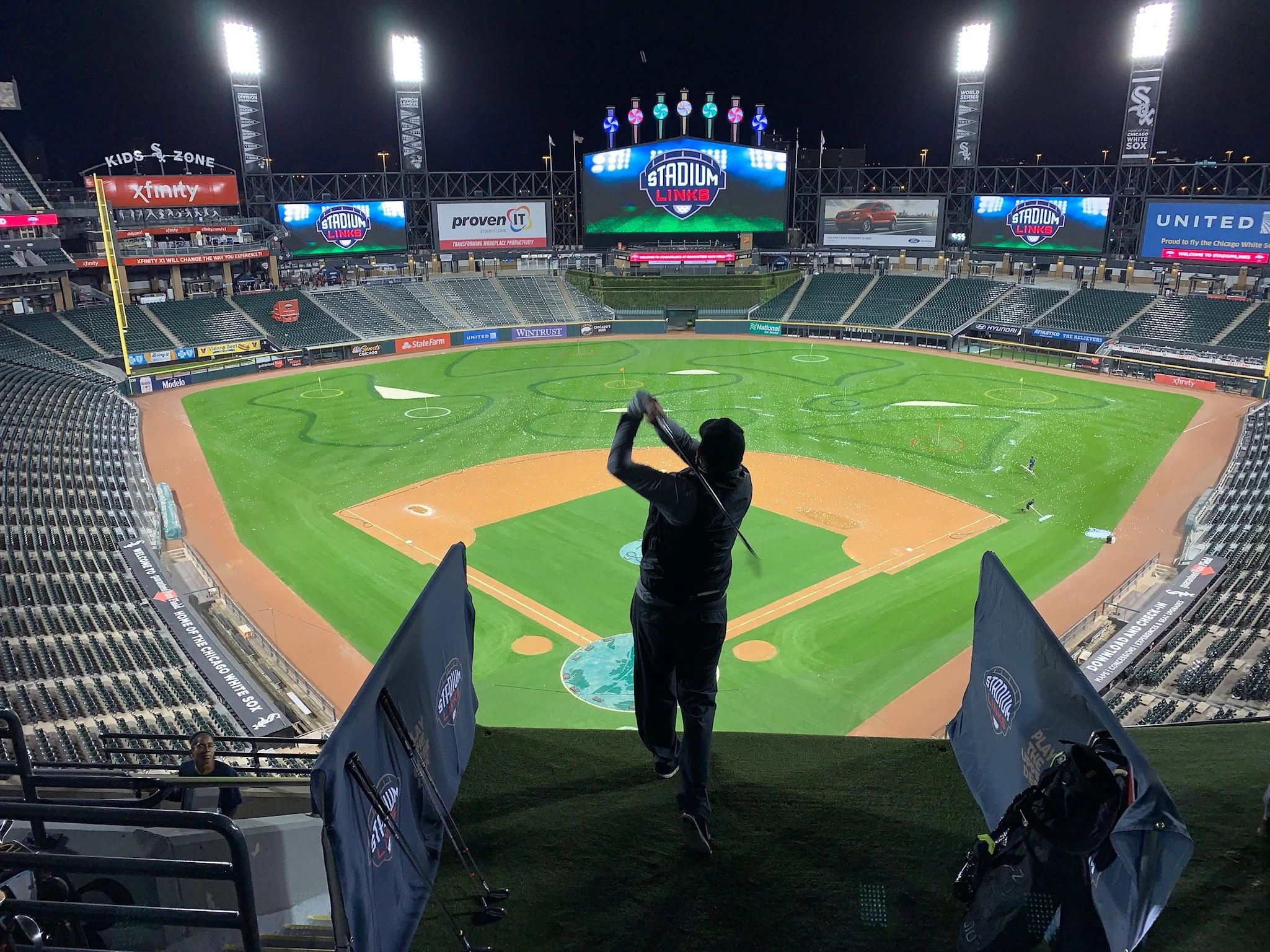 Person practicing golf on a field at night in a stadium.