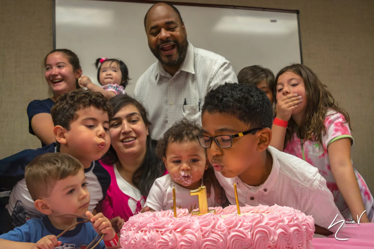 Children blowing out candles on a birthday cake with family gathered around