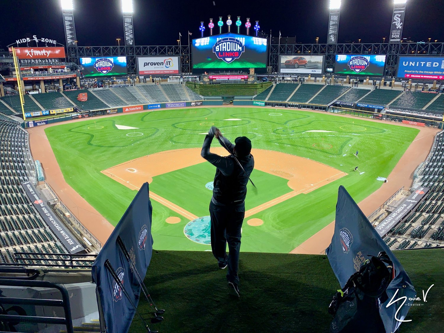 A person photographing the illuminated baseball field from the stadium seating
