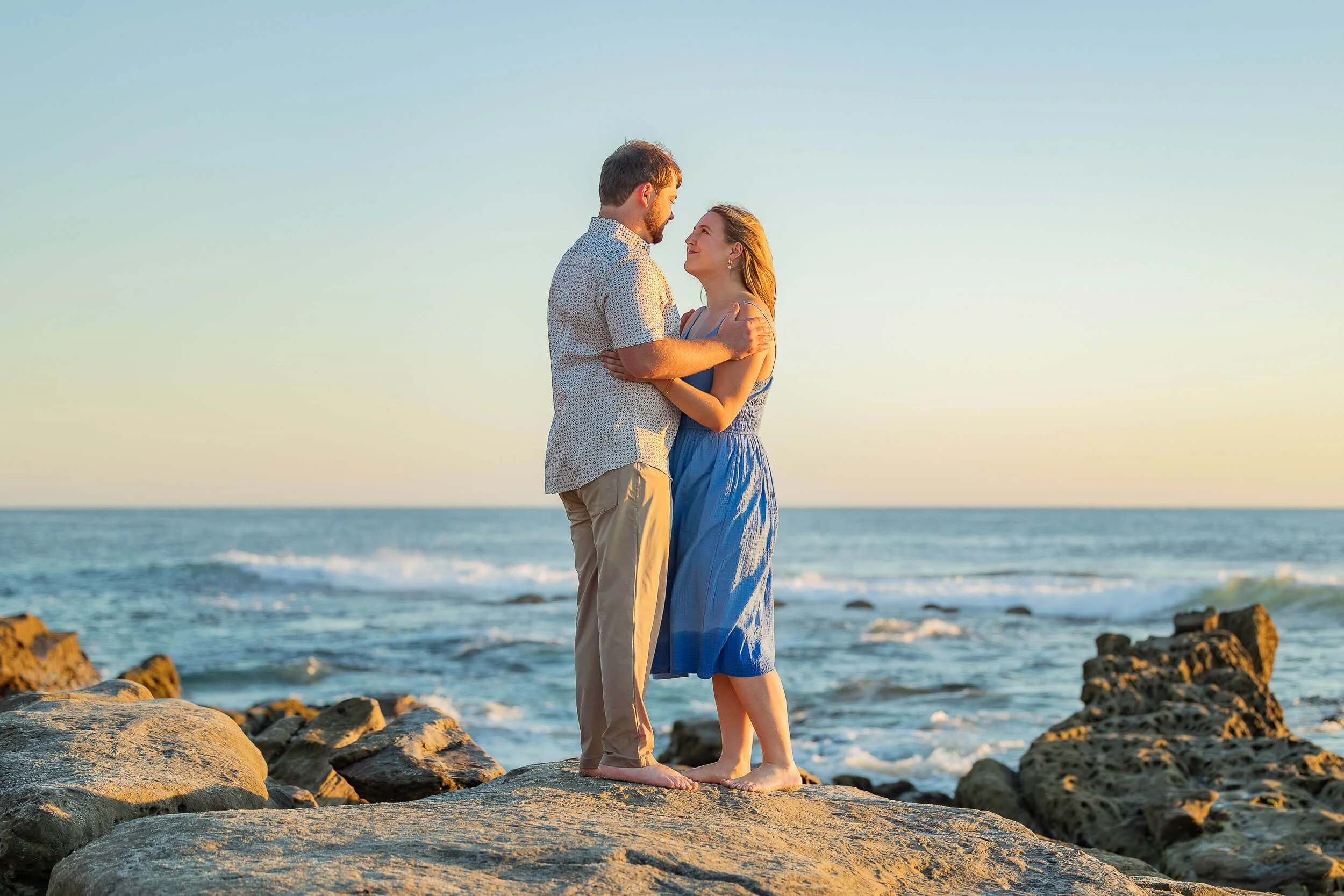 A couple embracing on a rocky beach at sunset.