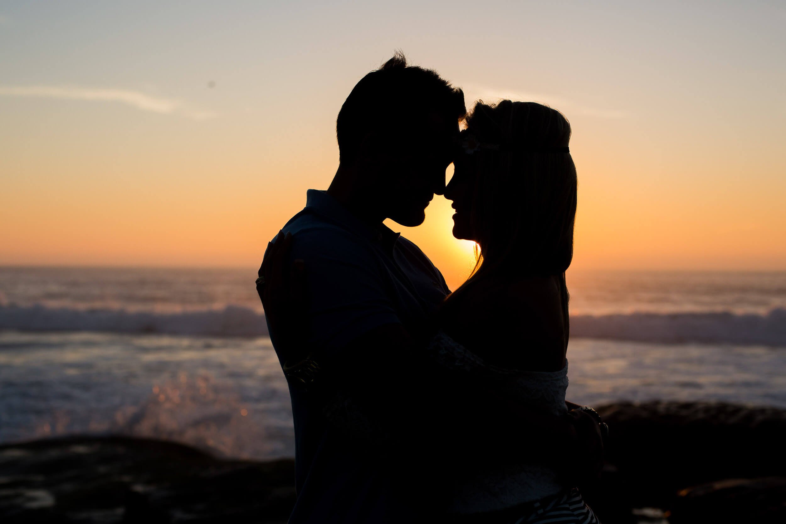 Silhouetted couple embracing at sunset on the beach, near the ocean waves.