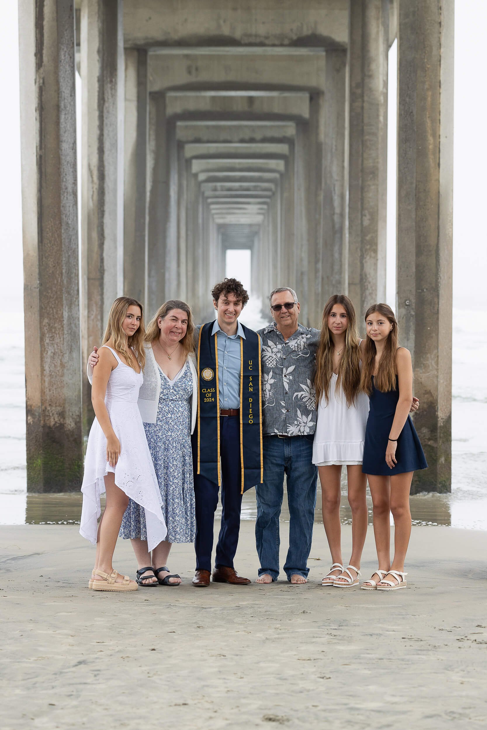 Family celebrating a graduation under a pier on the beach.