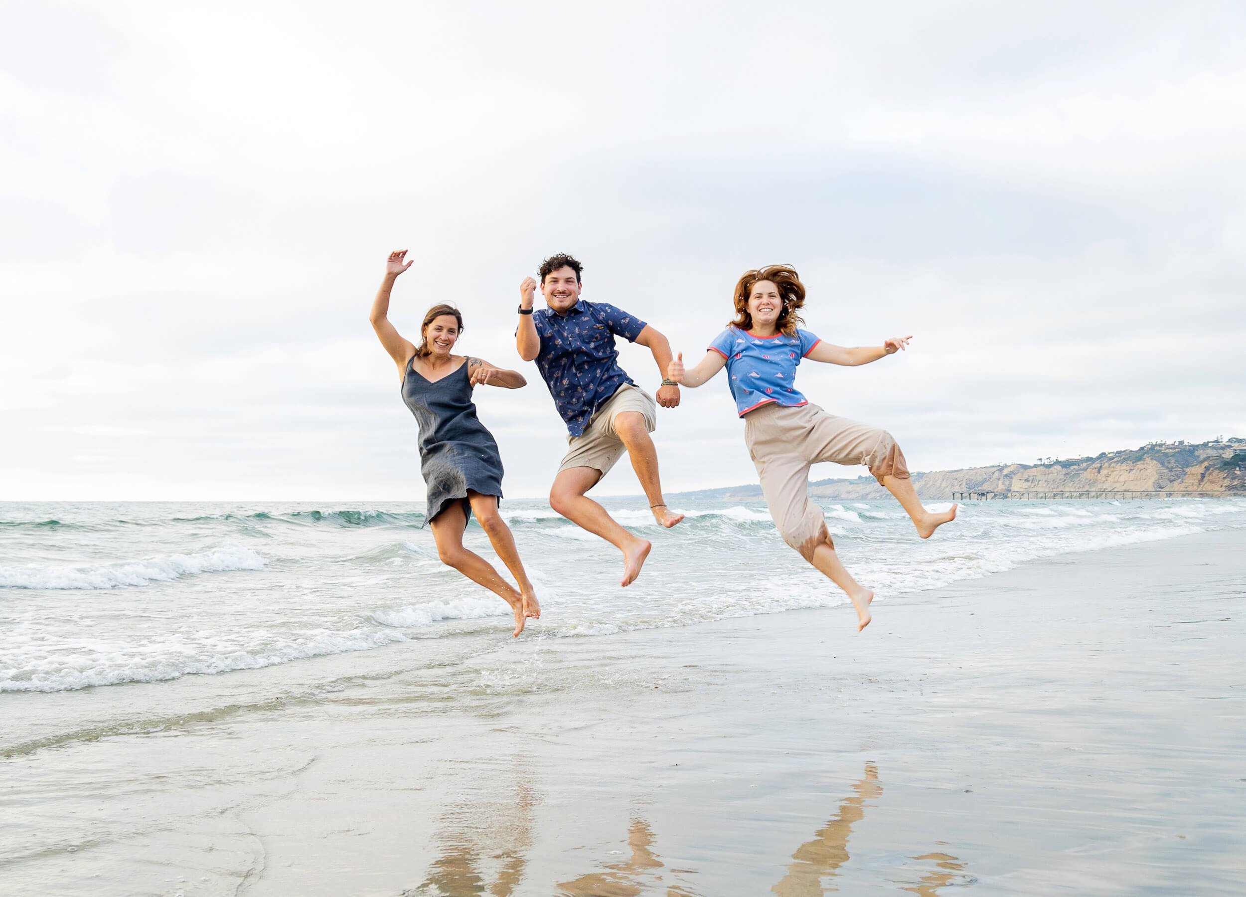 Three friends jumping on the beach near the water, smiling and having fun.