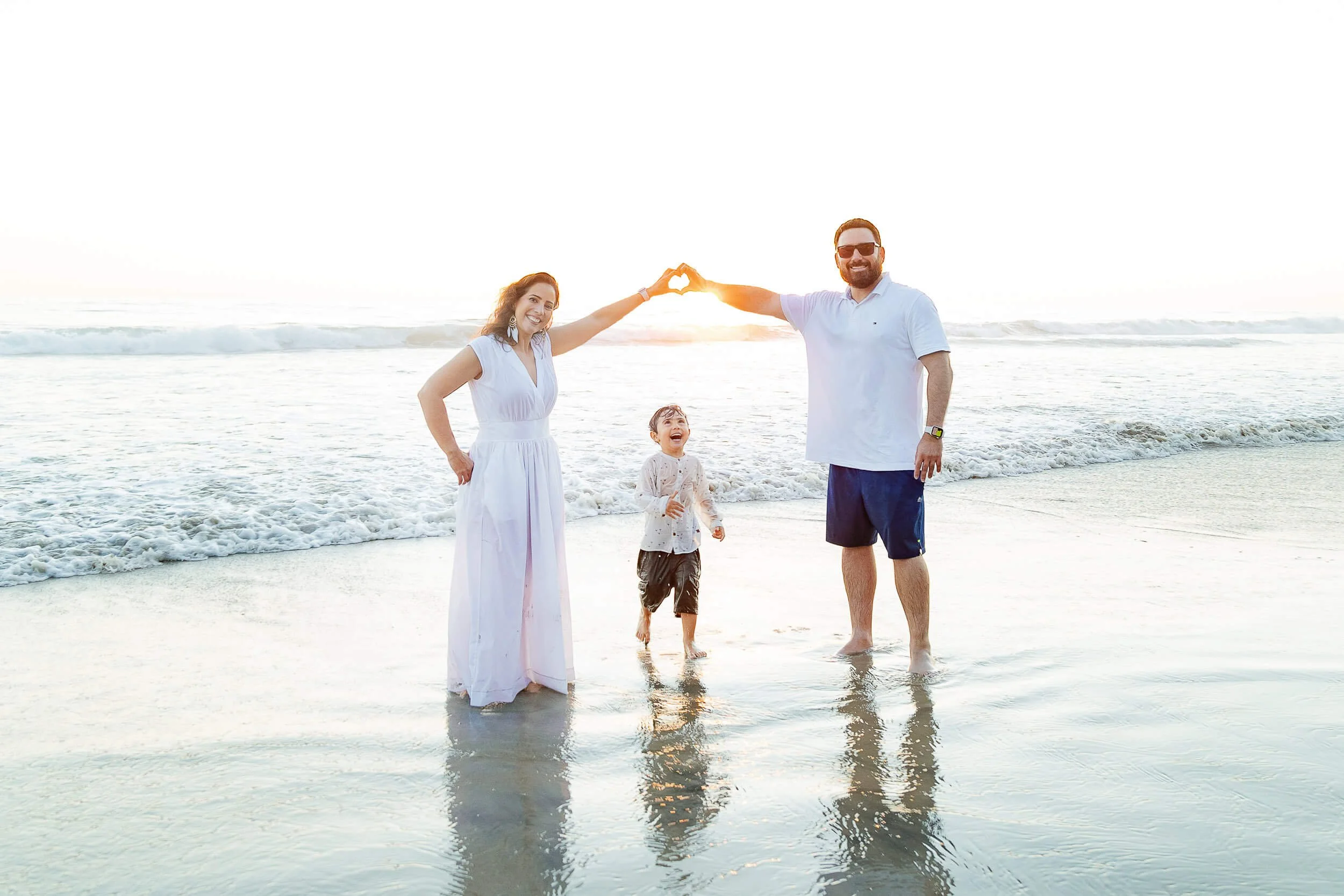 Family at the beach making a heart shape with their hands during sunset.