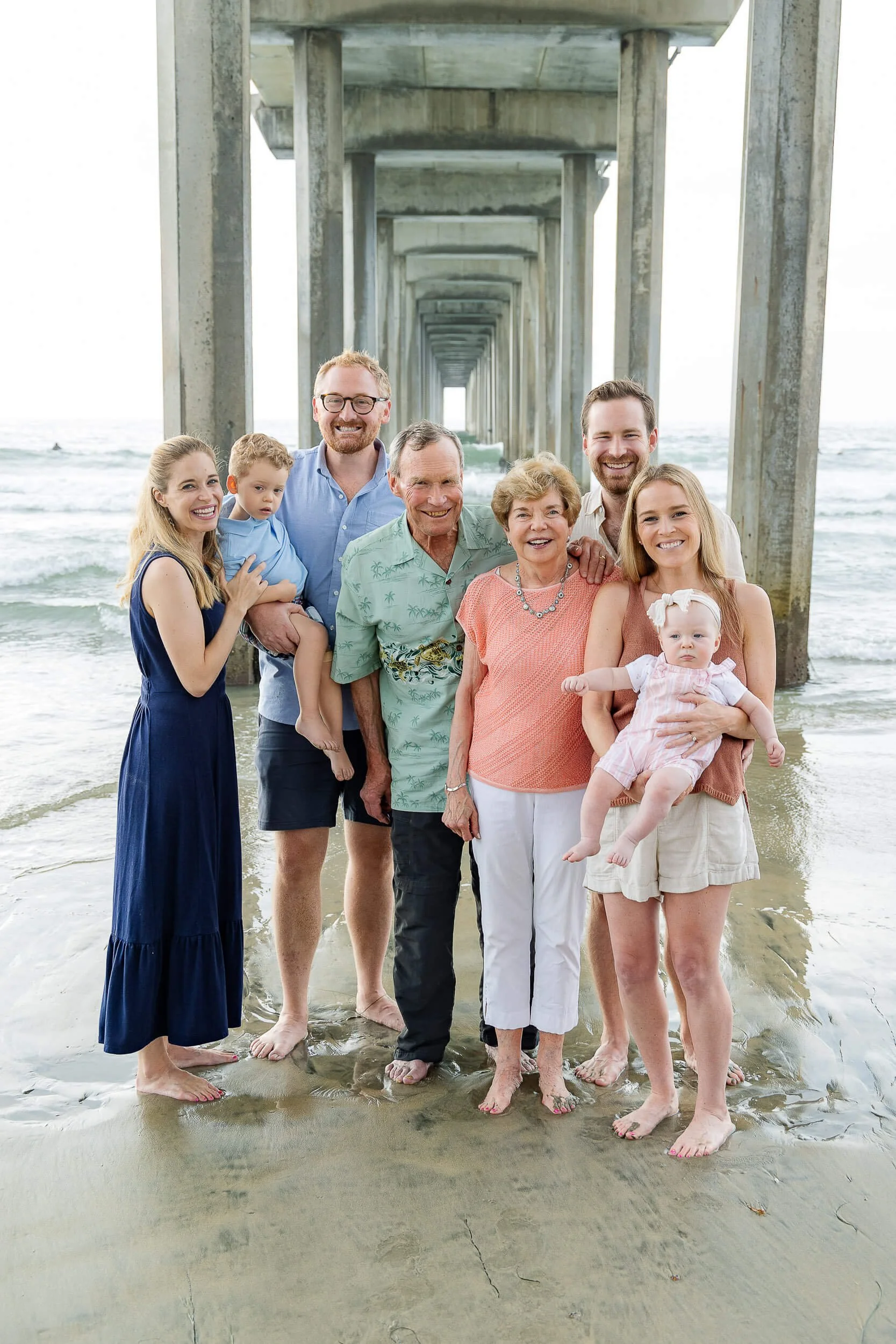 Family of nine in beach under a pier, smiling at the camera.
