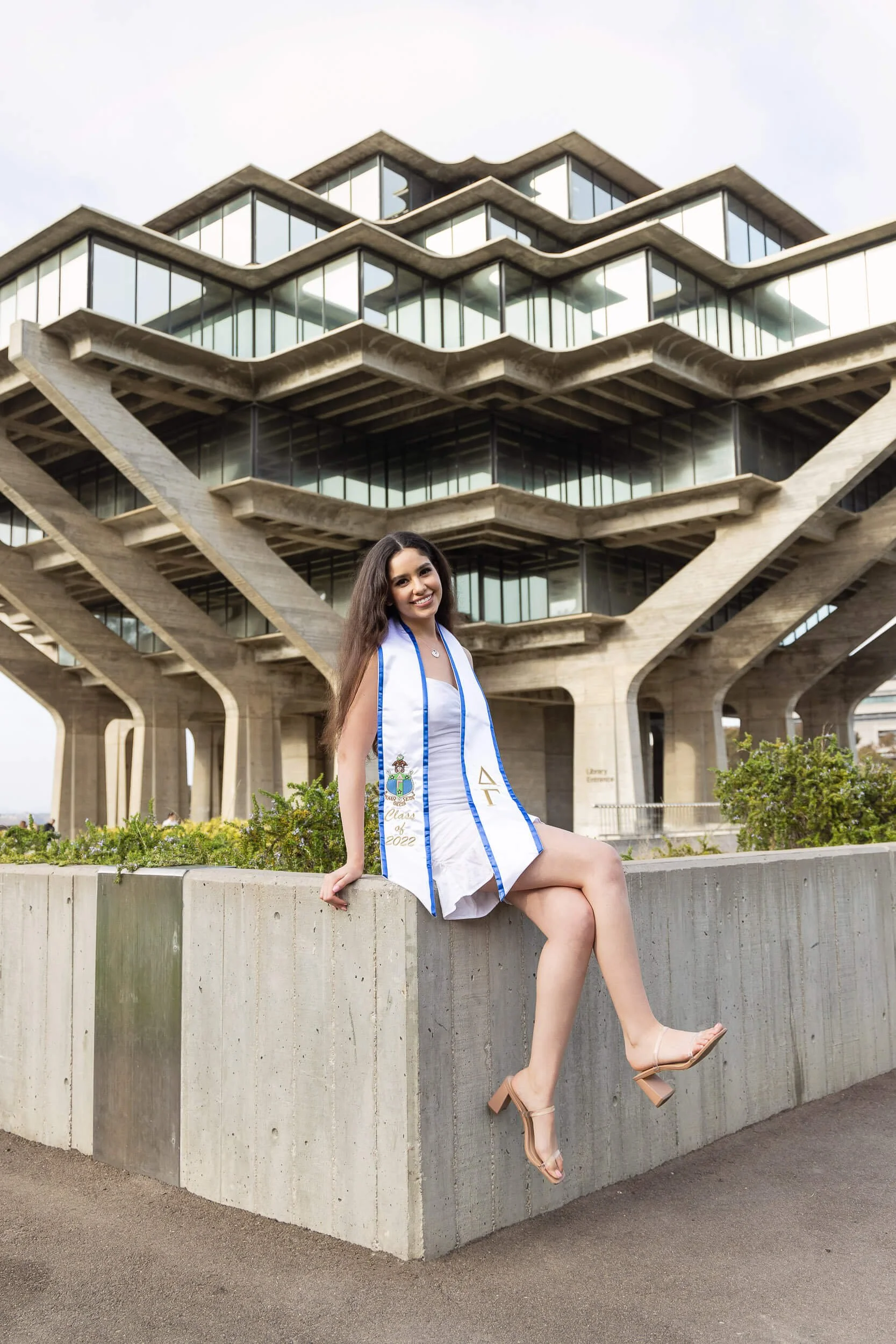 Graduation woman sitting on concrete ledge outside building.