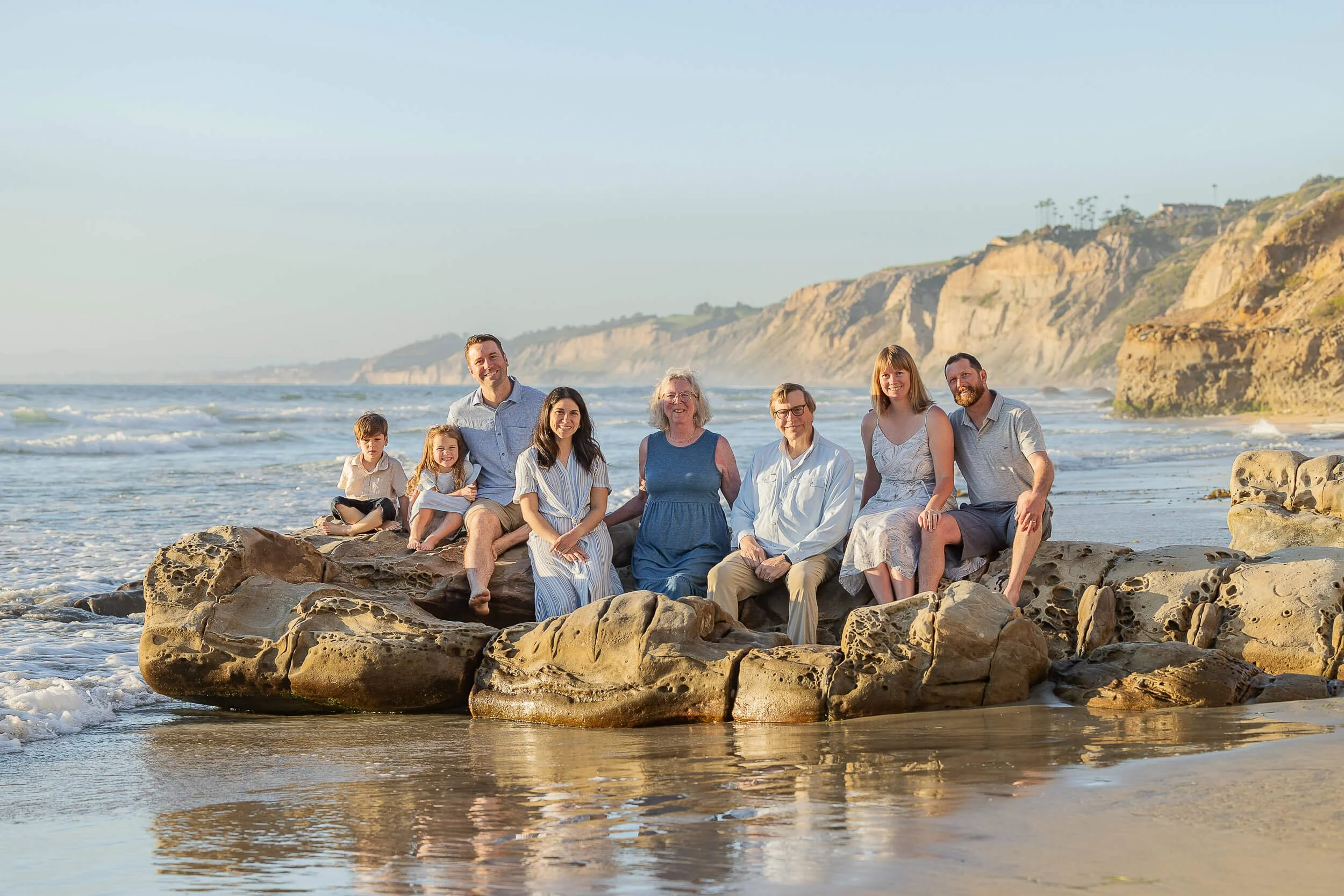 A large family sitting on rocks at the beach during sunset, with cliffs in the background.