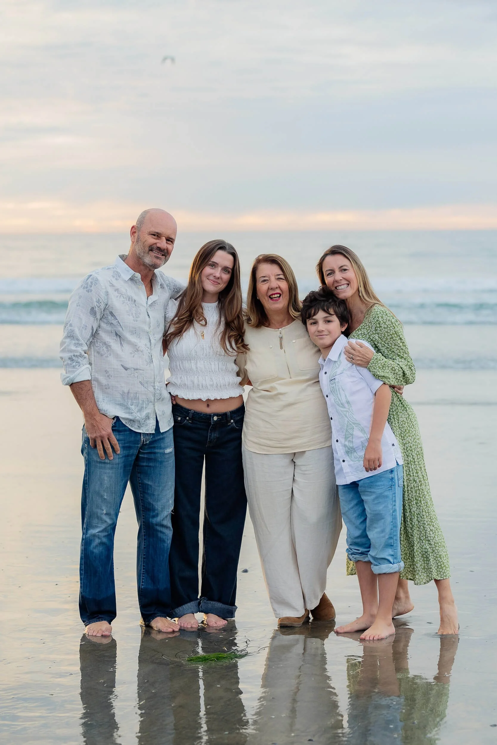 Family of five standing on the beach at sunset, smiling, with waves in the background.