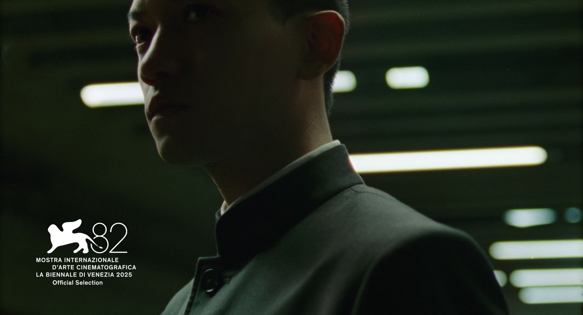 A man wearing a tuxedo in a dimly lit parking garage with fluorescent lights. The Venice International Film Festival 2025 official selection logo is in the bottom left corner.
