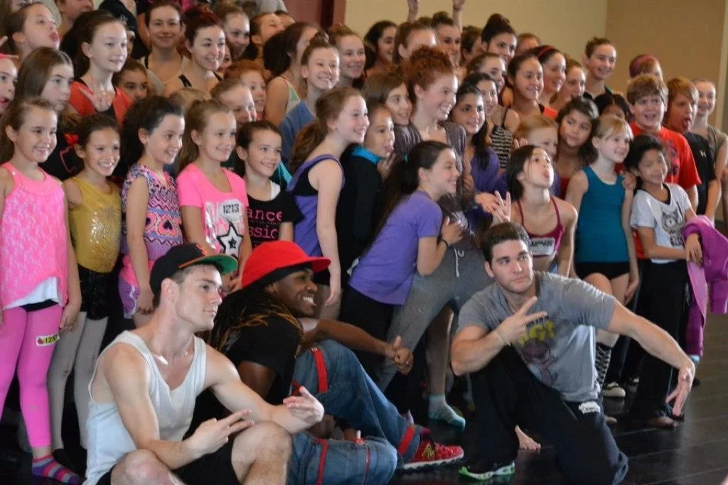 Group of smiling young girls and three adult men posing for a photo in a dance studio or gym.  Matt Marr Teaching at Dance Convention