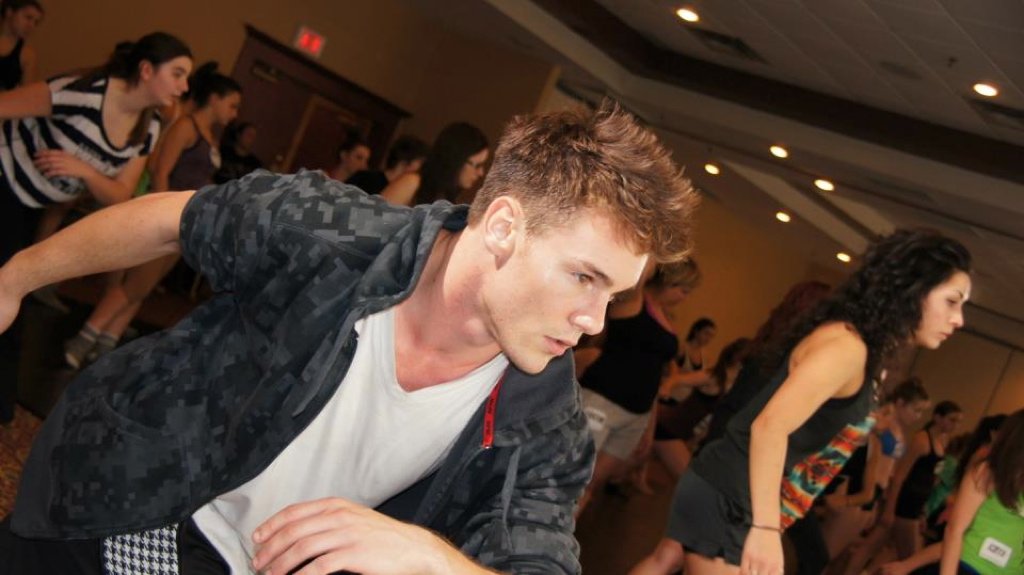 People participating in a dance or exercise class in a large room, focused and moving in unison.  Matt Marr Teaching at Dance Convention.
