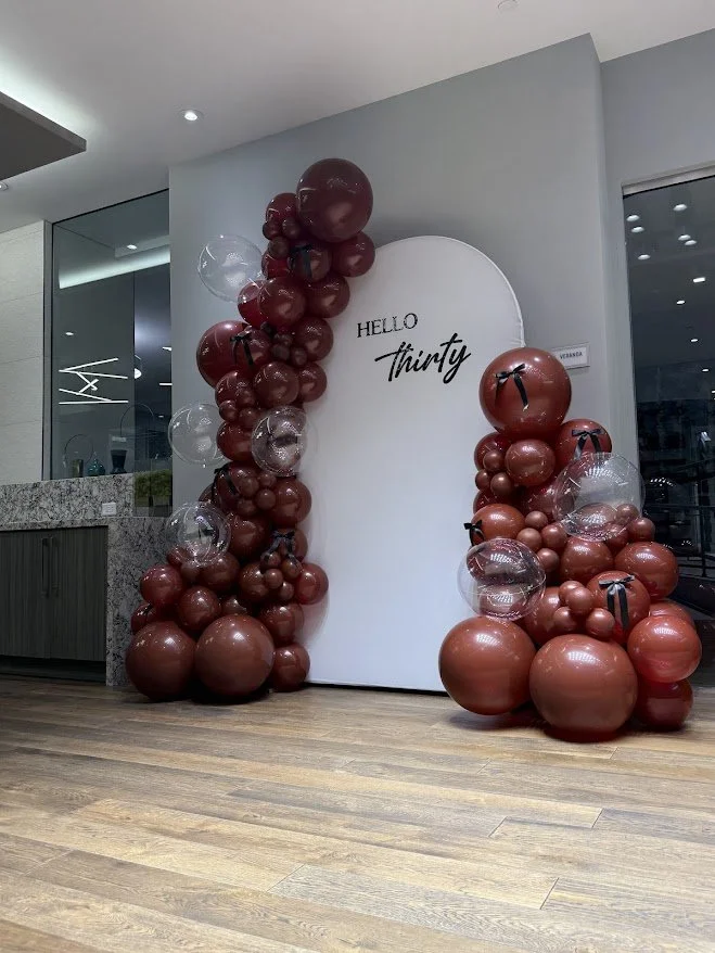 Decorative balloon arrangement with red and clear balloons surrounding a white backdrop that says 'Hello Thirty'.
