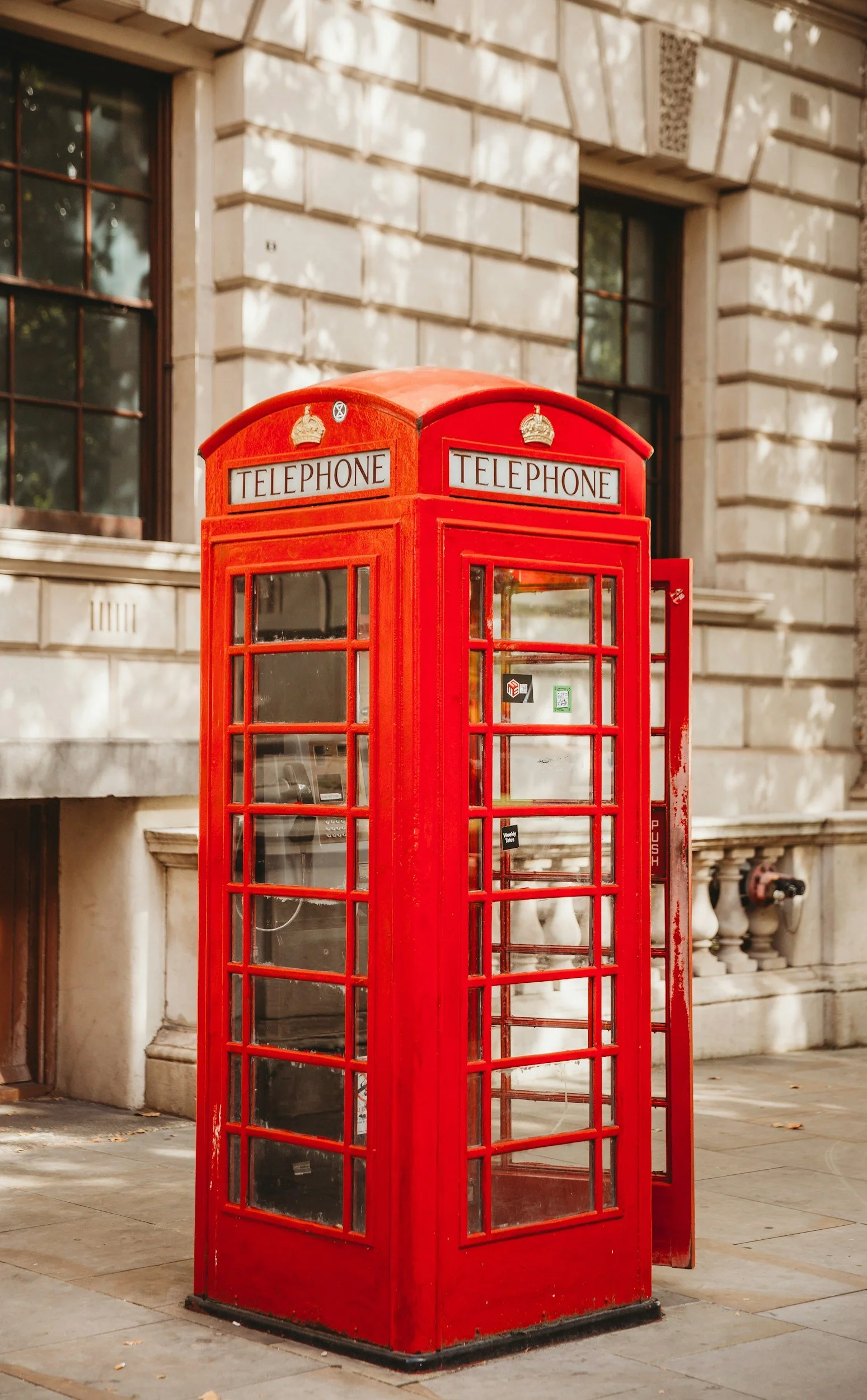 Red British telephone booth on street sidewalk in front of a stone building