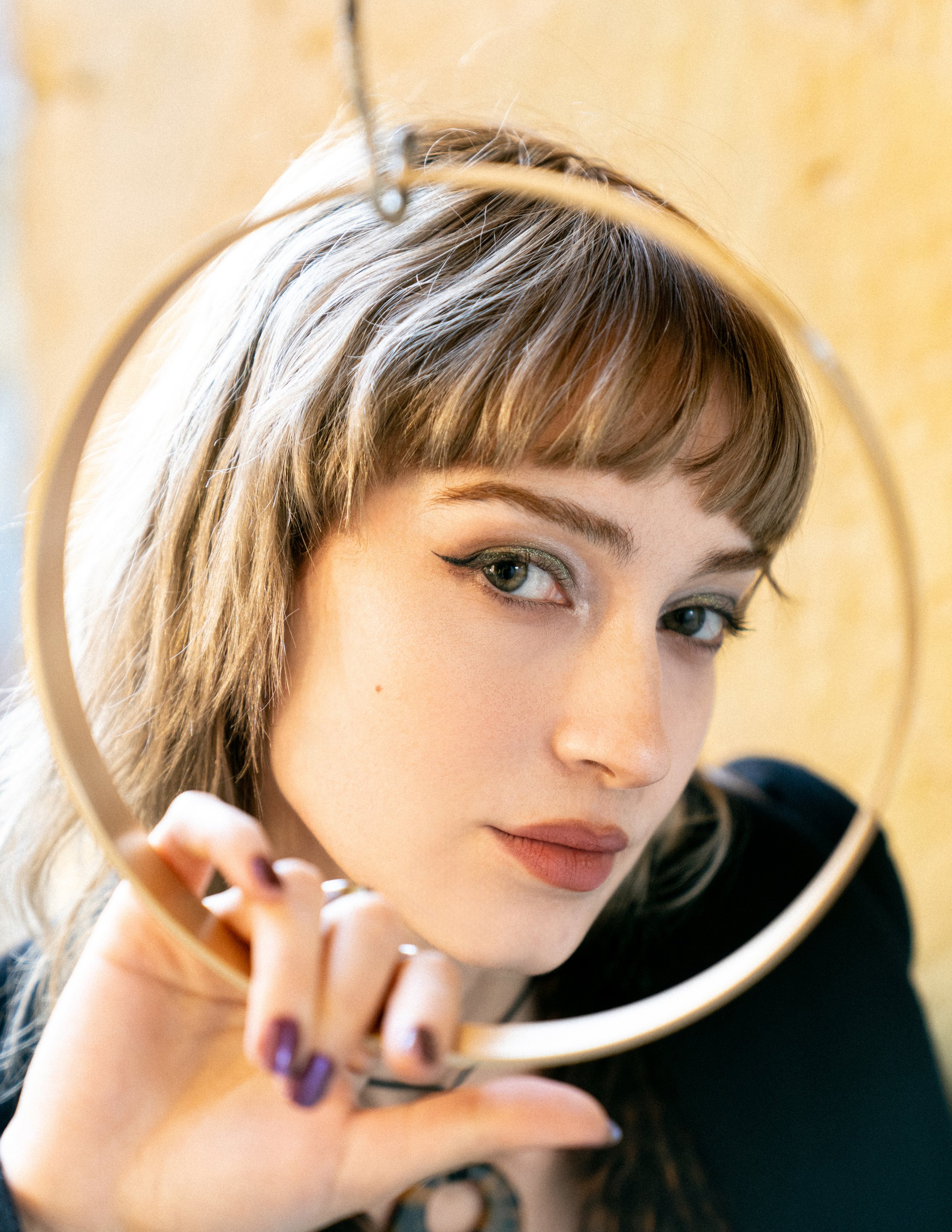 A woman holding a round mirror, looking at her reflection.