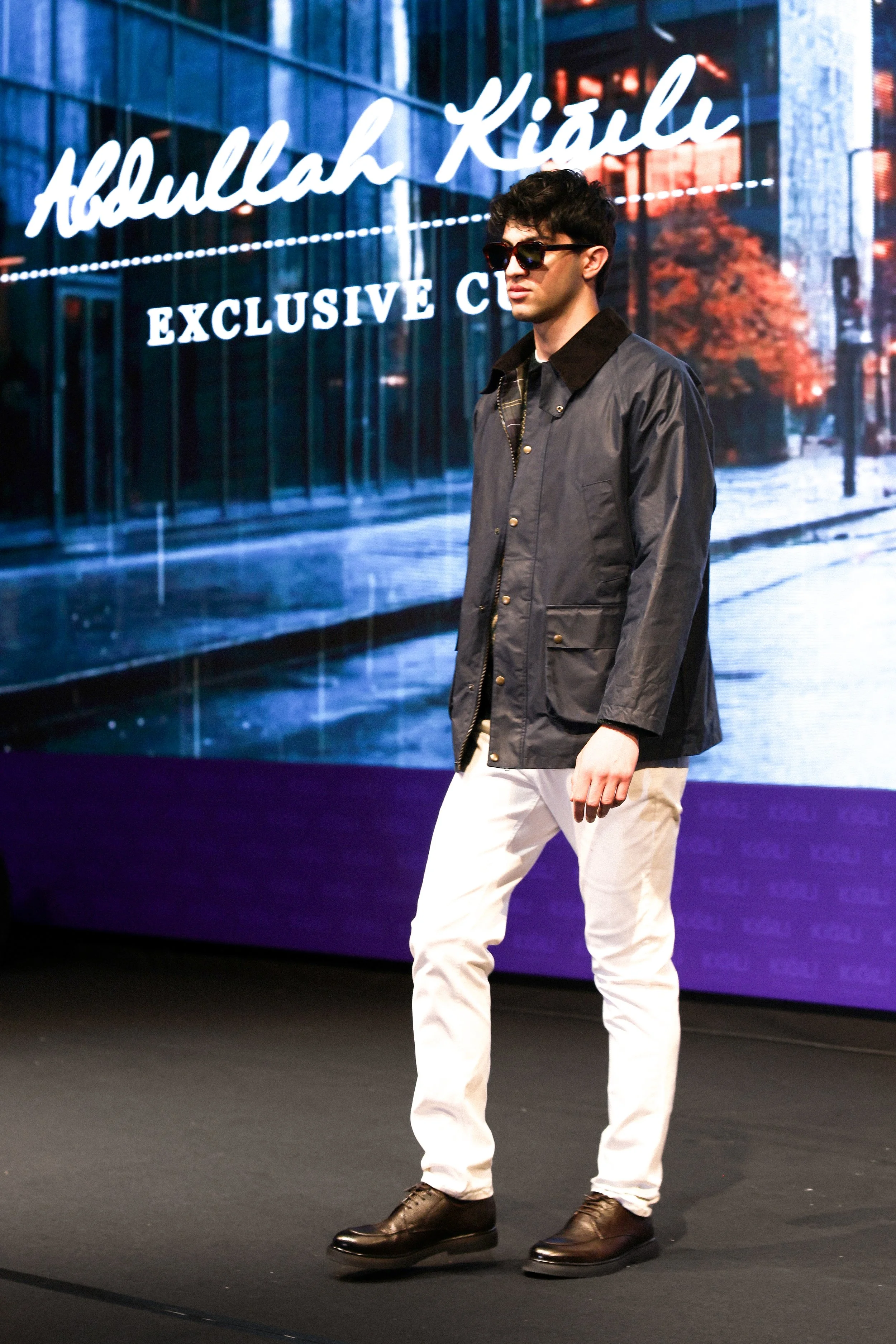 Young man walking on stage in front of a backdrop with the name Abdelilah Kiarli and the words 'Exclusive Club'.