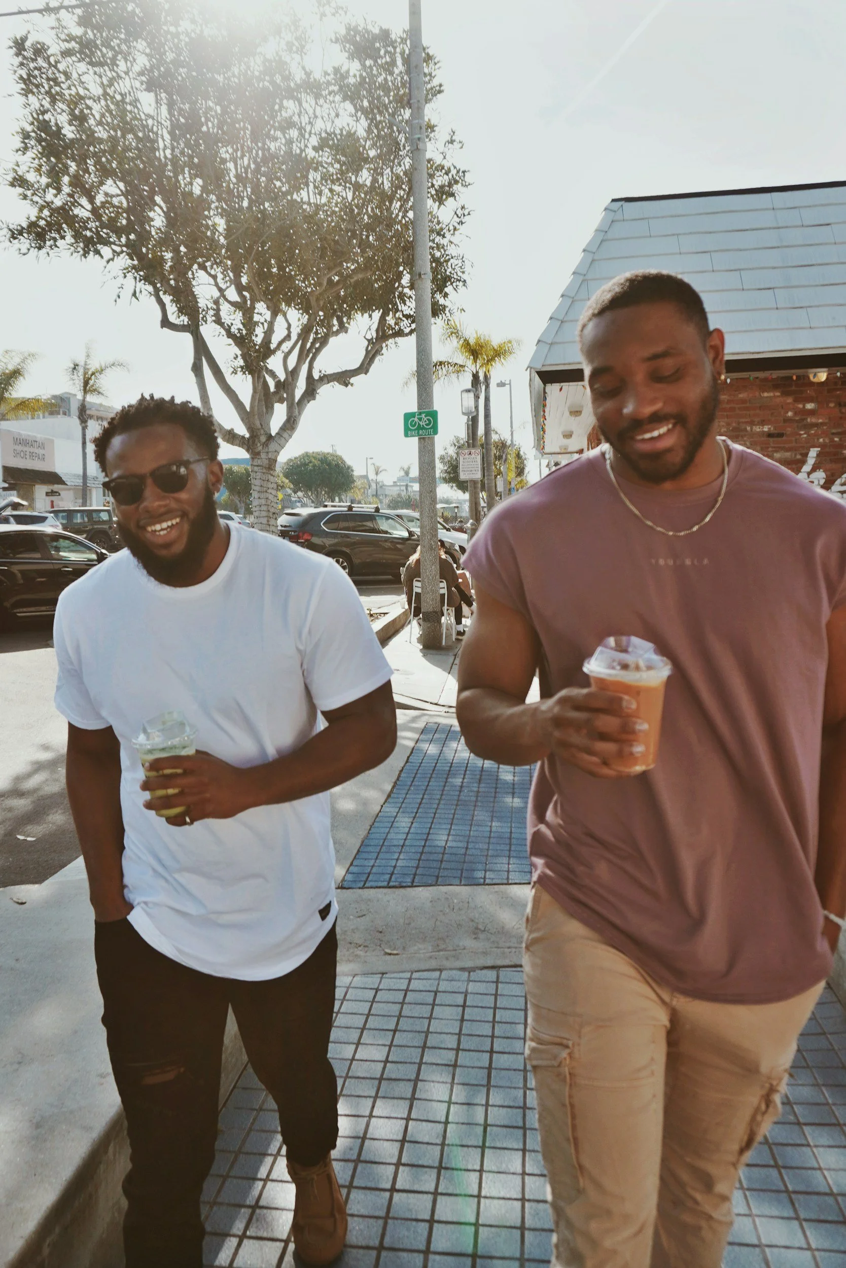 Two young men walking outdoors in a sunny urban environment, each holding an ice cream cone, smiling and enjoying their time.