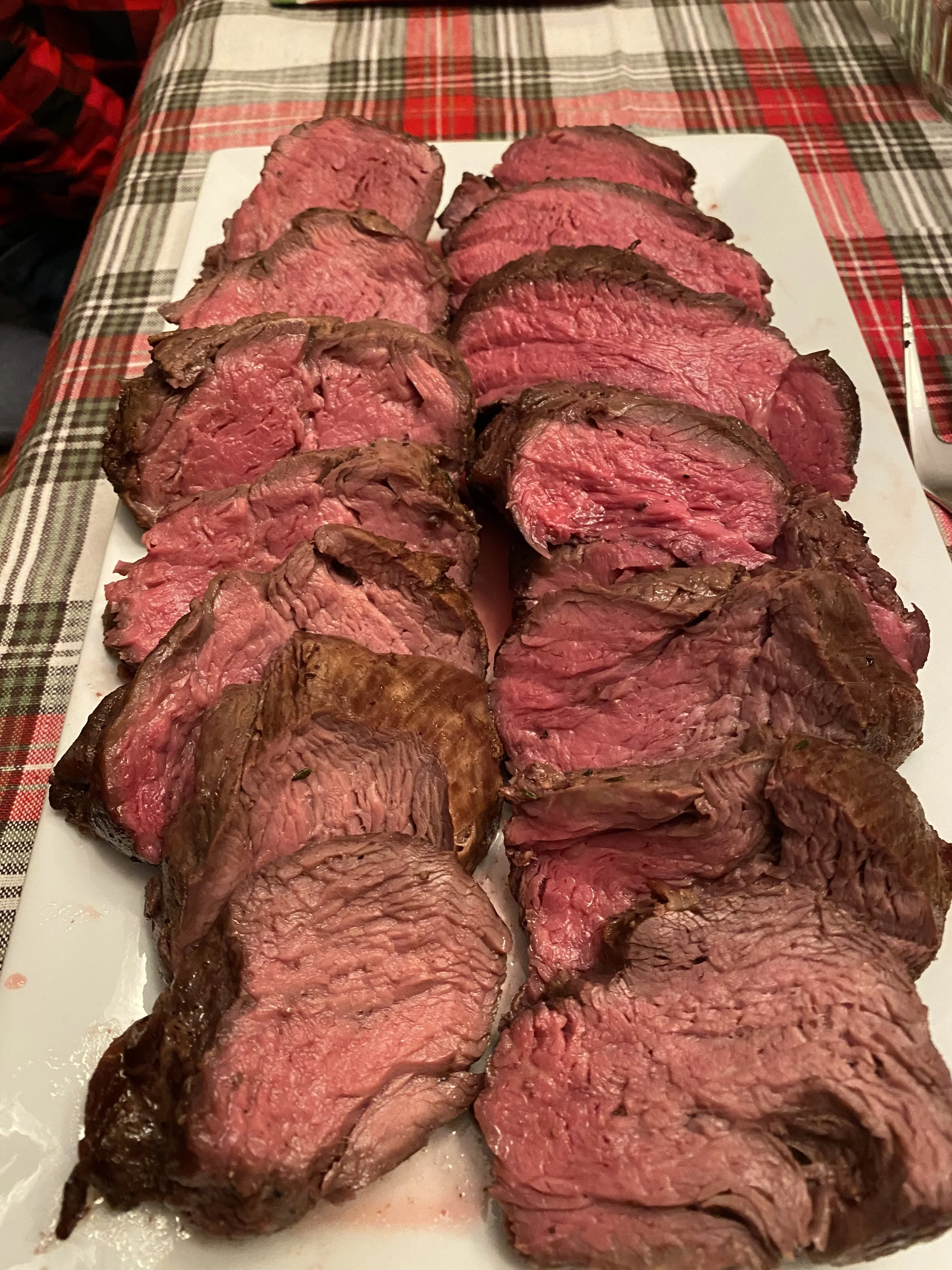 Sliced cooked beef roast on a white platter set on a table with a plaid tablecloth.