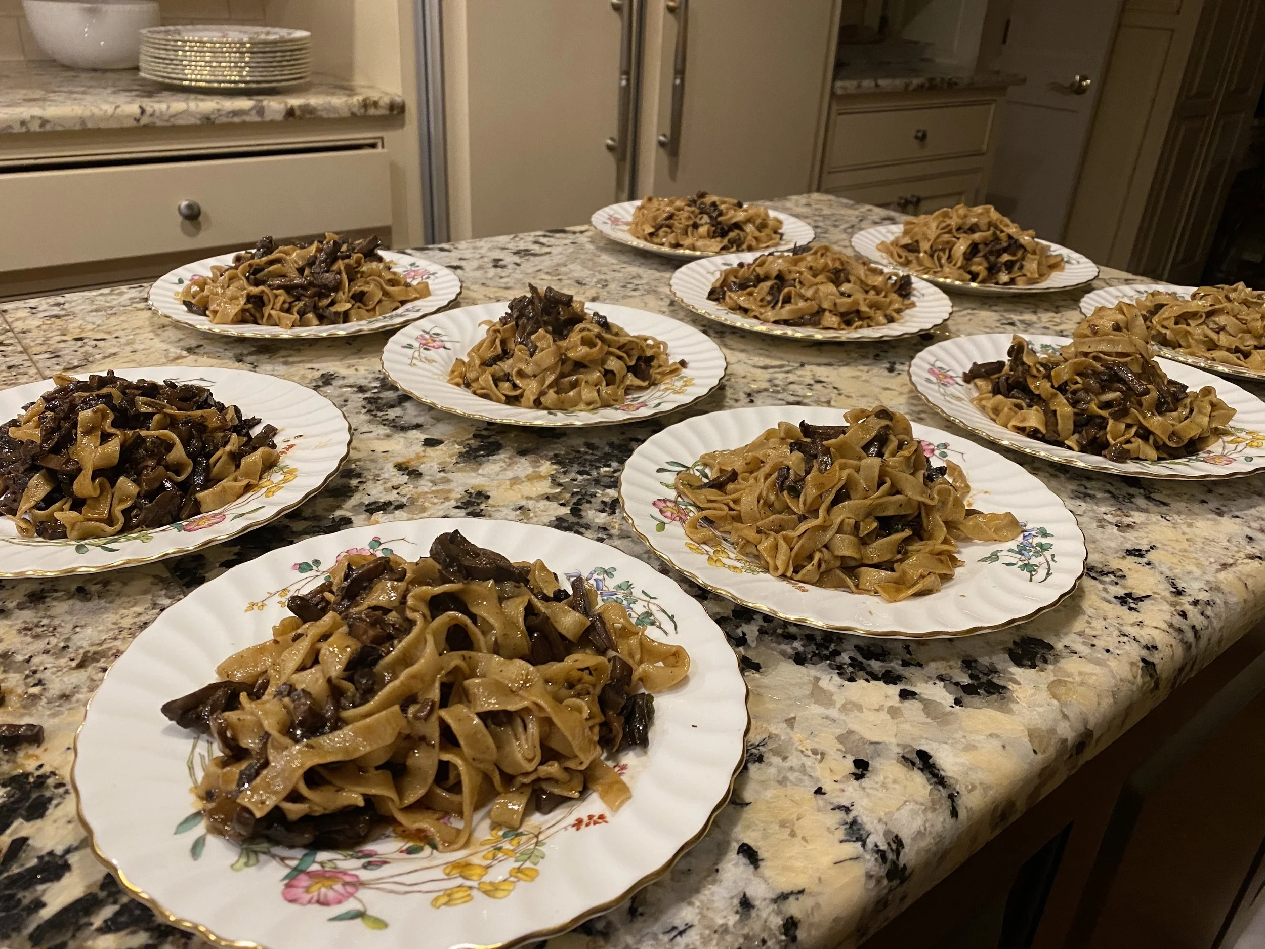 Several plates of cooked pasta with dark sauce on a kitchen countertop.